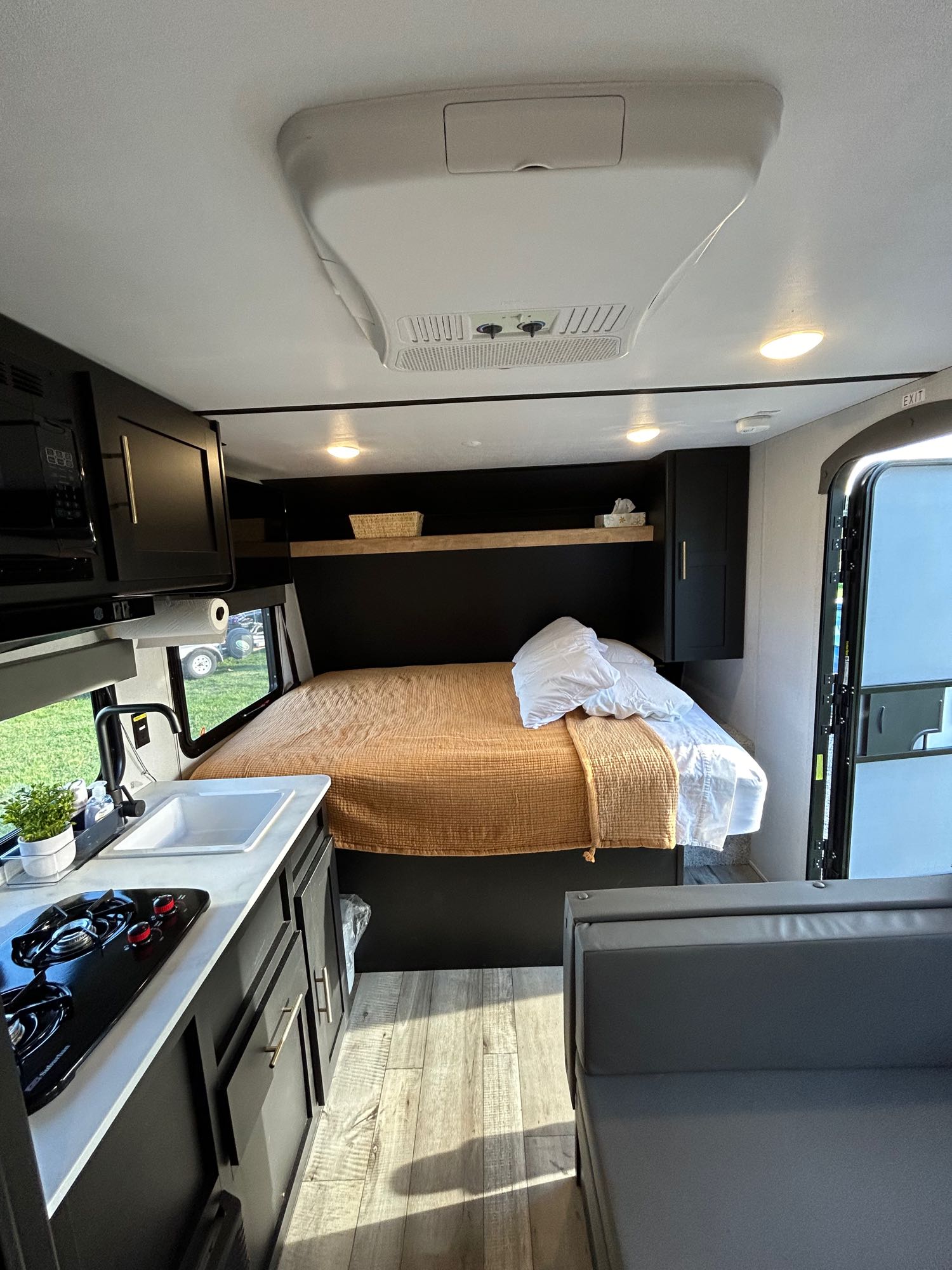 This modern **RV rental** interior showcases a compact kitchen, comfortable bed with white pillows, and grey sofa. Ready for your adventure!. Keystone RV Springdale 2022
