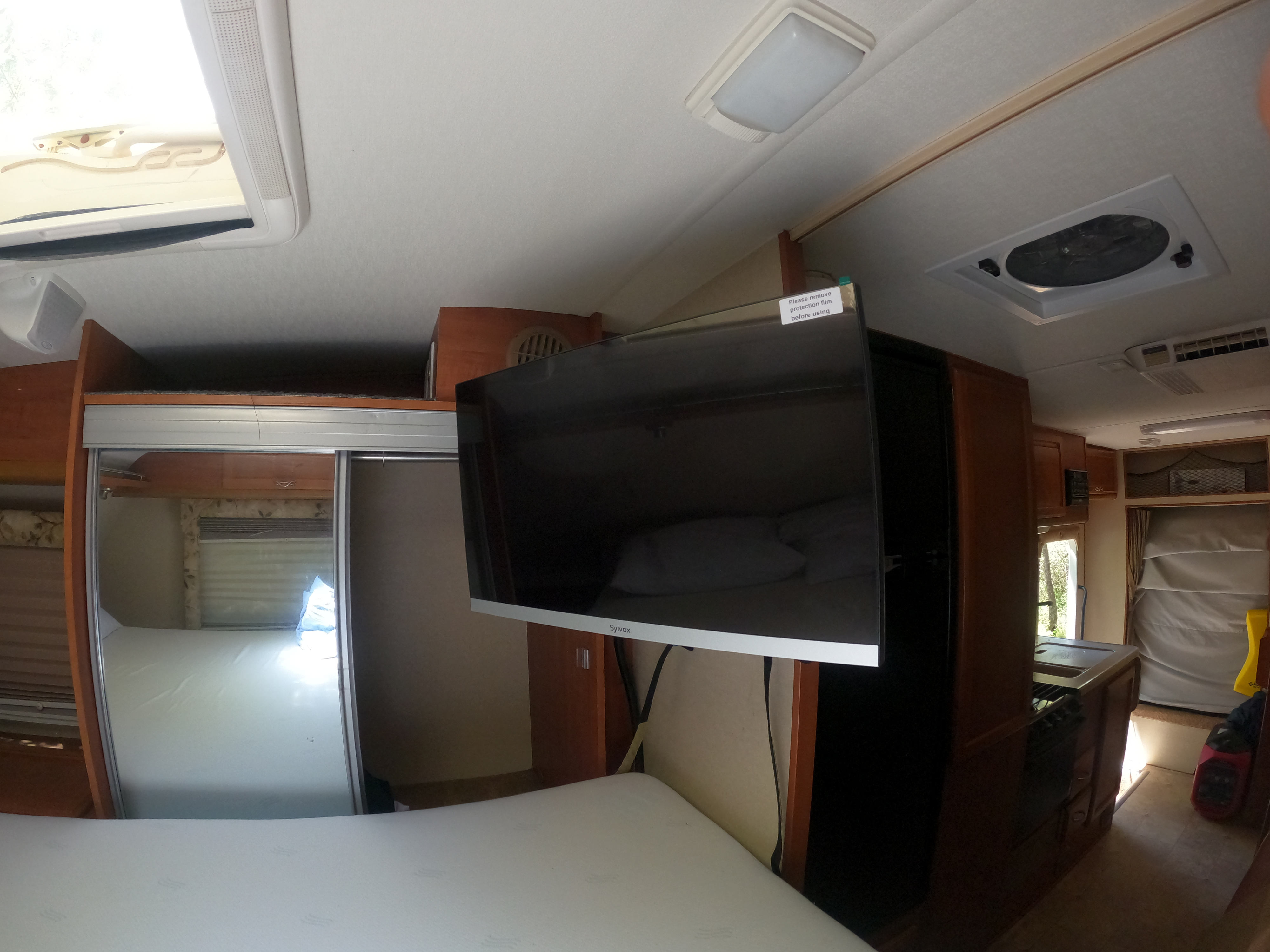Inside this RV rental, a compact bedroom features a bed, mounted TV, and mirrored closet, offering a glimpse of the kitchen.. Lance 1191 2012