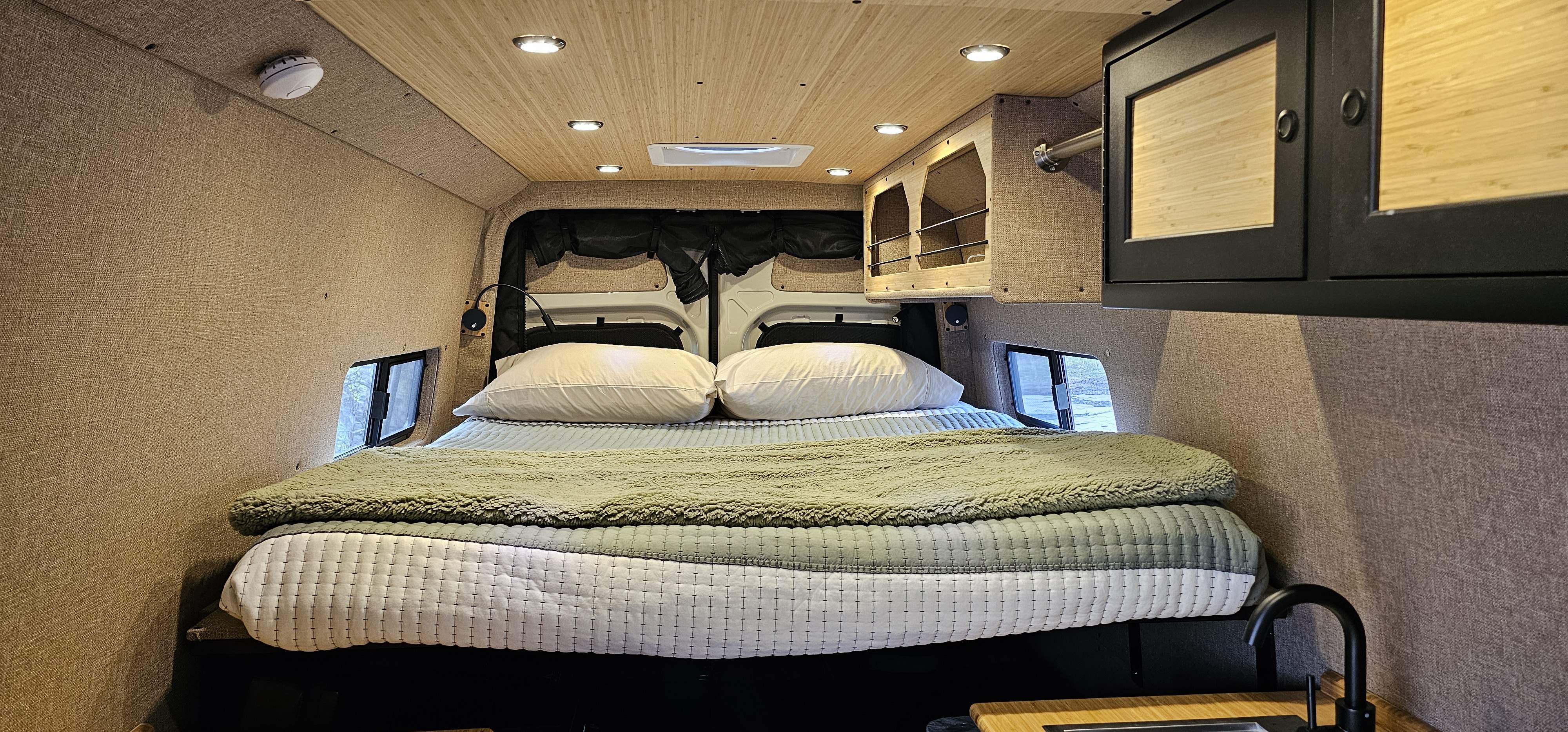 Cozy RV rental interior featuring a comfortable bed, overhead storage, side windows, and a compact kitchen sink.. Mercedes-Benz Sprinter RV Motorhome Campervan 2023