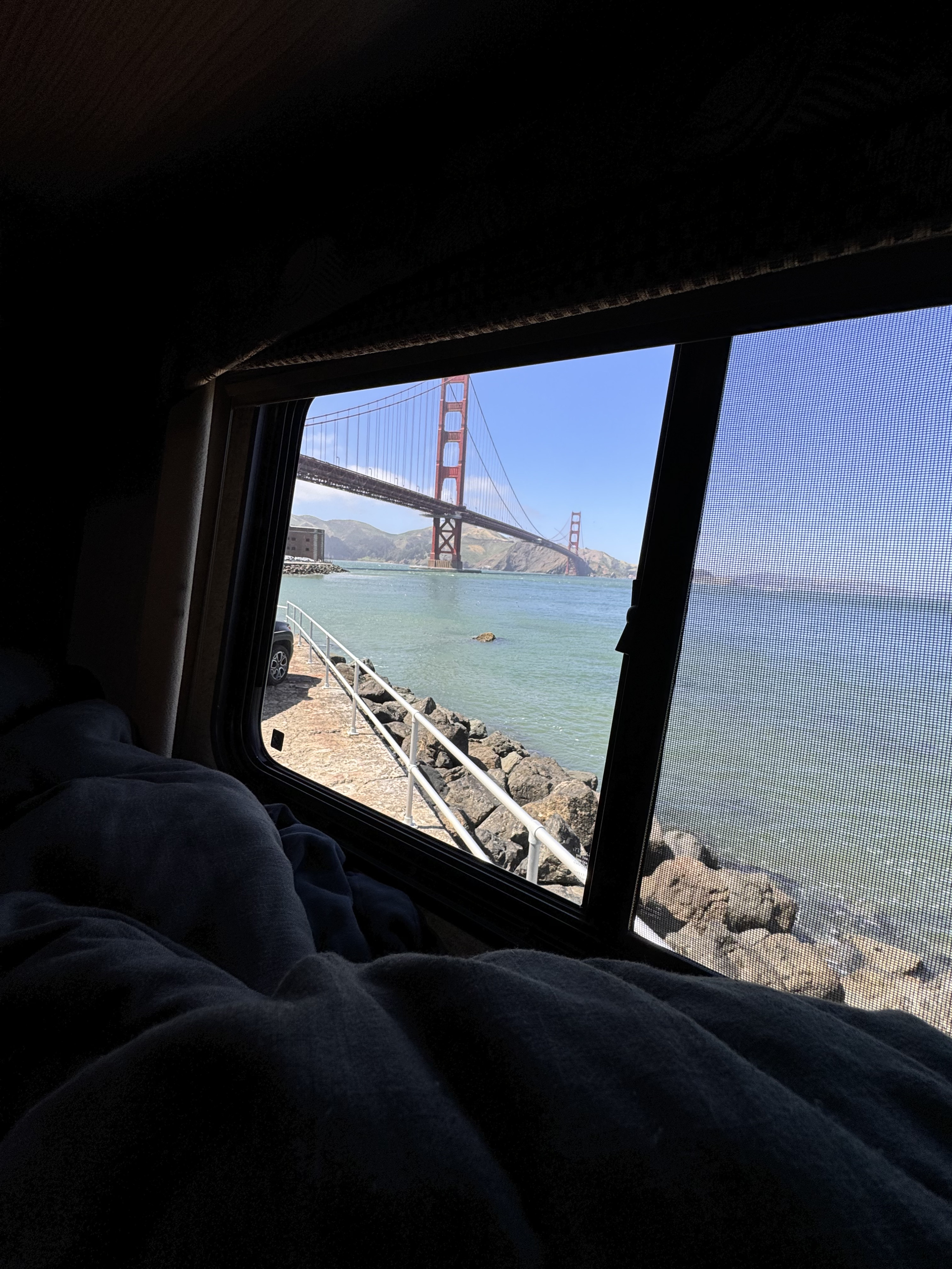 Cozy RV rental view of the iconic Golden Gate Bridge over the bay, seen from a bed with dark blankets.. Ford Ford Transit 2018