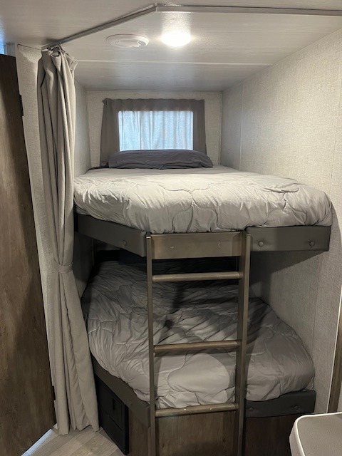 An RV rental's sleeping area featuring comfortable bunk beds with gray bedding, a ladder, and a privacy curtain.. Forest River Salem Cruise Lite 2021