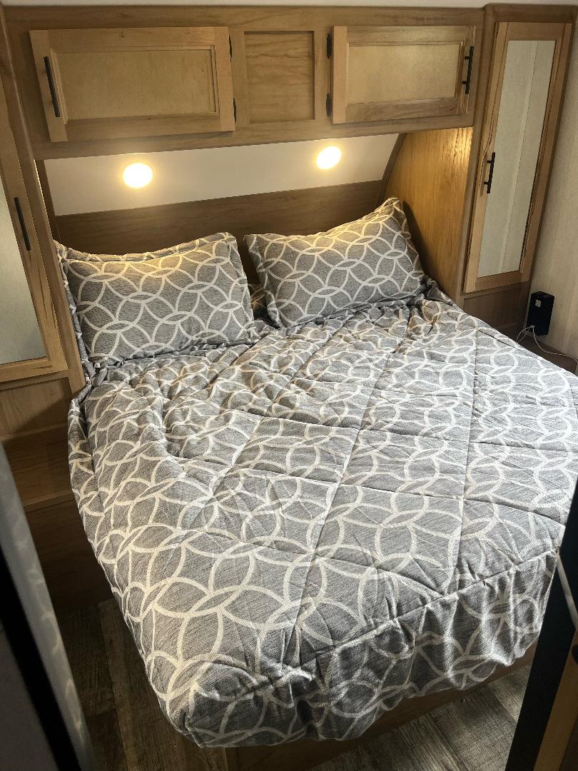 Experience comfort in this RV rental bedroom, featuring a neatly made bed, ample storage, and reading lights.. Forest River Cherokee Grey Wolf 2023