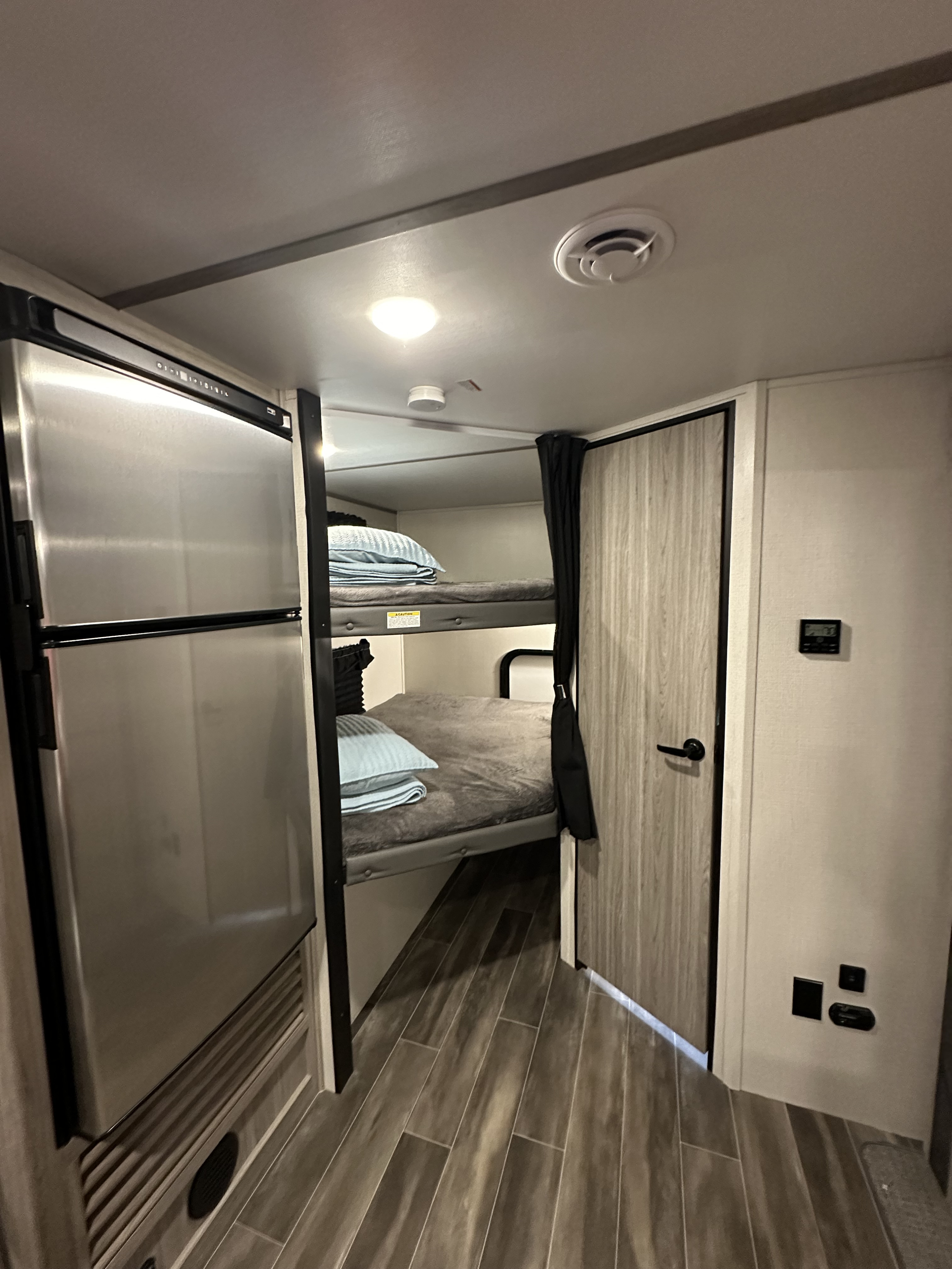 RV rental interior featuring comfortable bunk beds next to a stainless steel refrigerator, ideal for mobile living.. Keystone RV Passport SL 2022