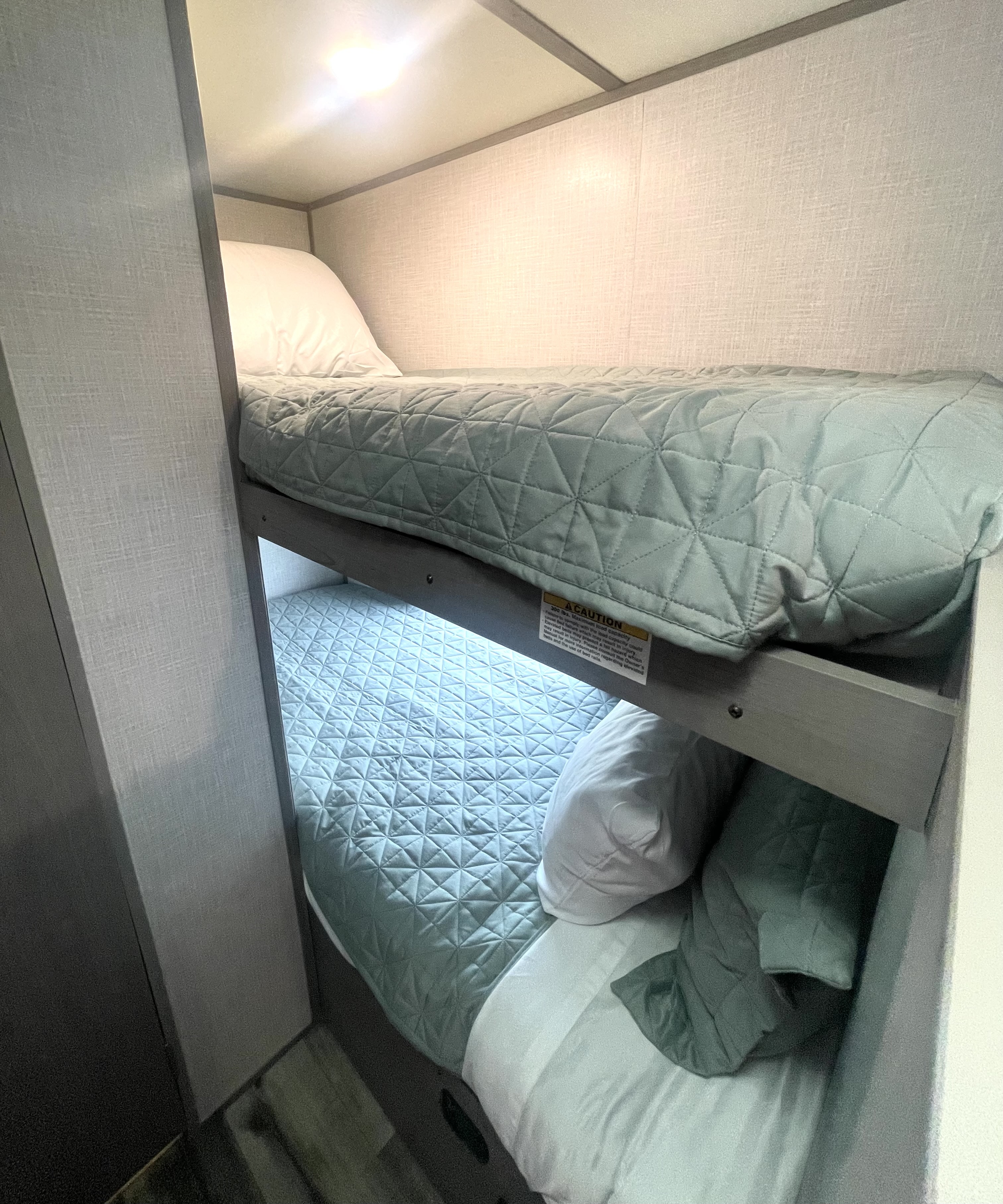 Comfy RV rental bunk beds feature light green quilted blankets and white pillows, perfect for travel adventures.. Dutchmen Coleman Lantern LT 2023