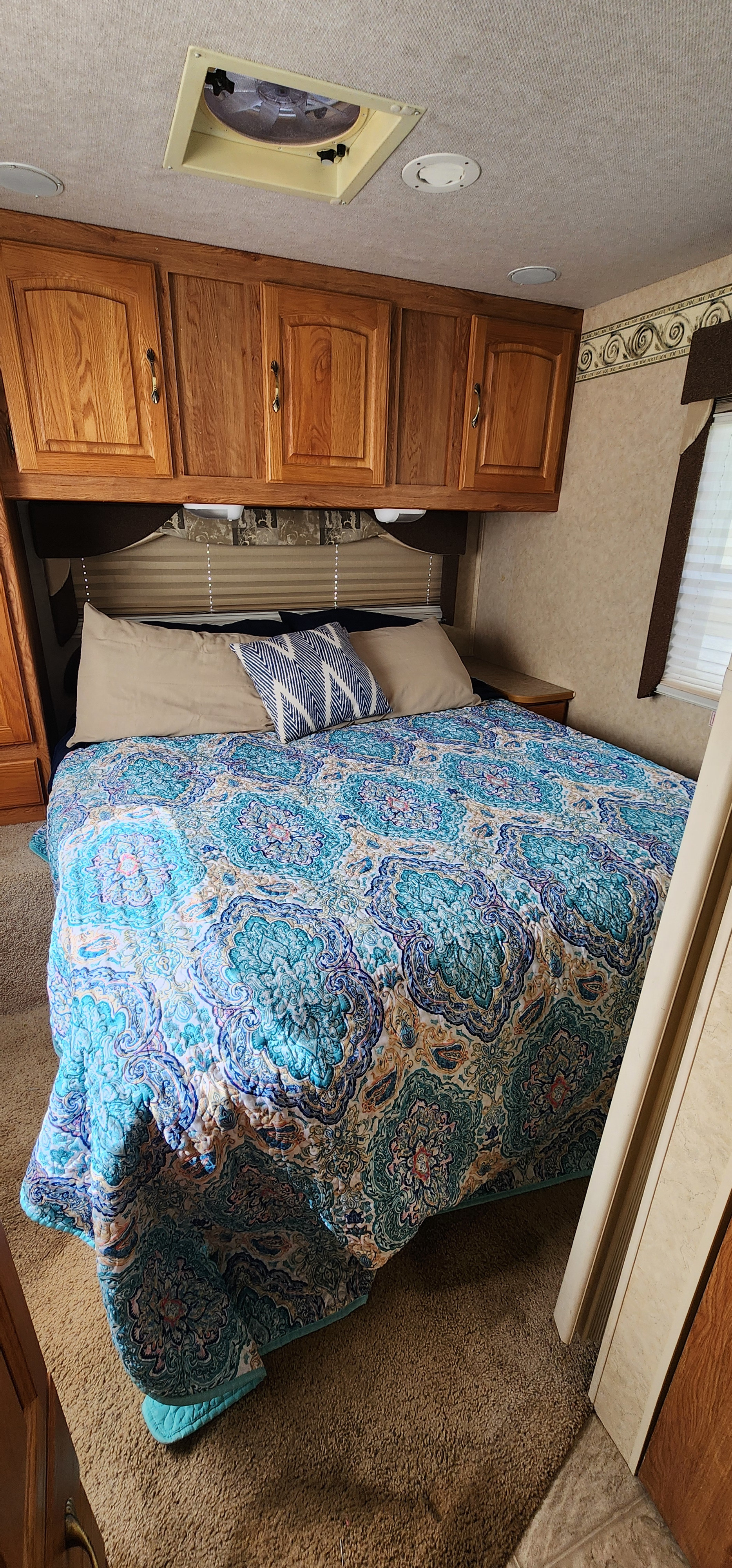RV rental: Compact bedroom with a vibrant blue patterned comforter, wood cabinets, and overhead vent.. Jayco Greyhawk 2006