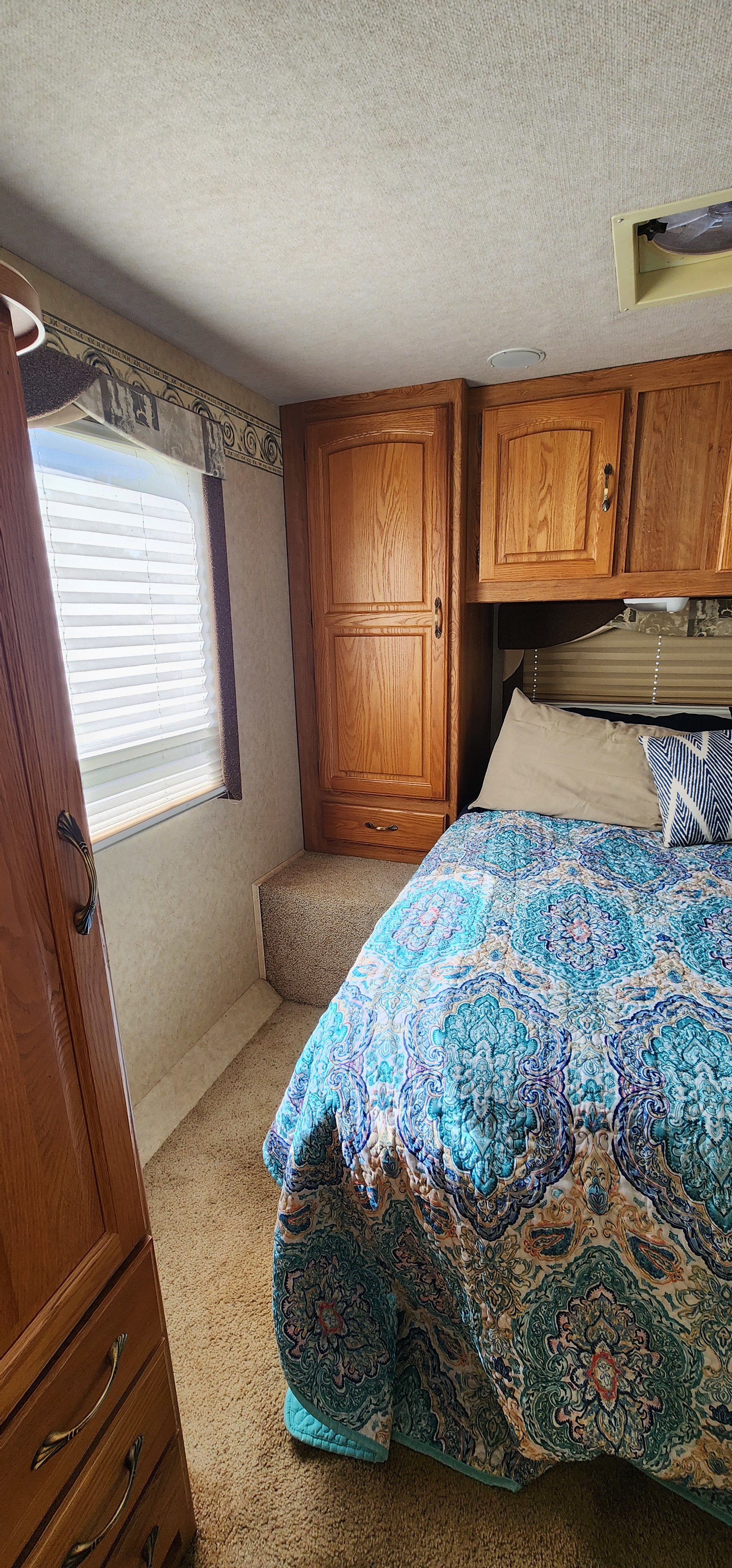 Inviting RV rental bedroom showing patterned bed, wood cabinetry, window, and carpeted step-up, ideal for travels.. Jayco Greyhawk 2006
