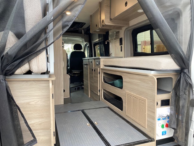 Modern RV rental interior showing a compact living space, complete with a bed/bench, storage, and a small sink area.. Winnebago Solis 2021