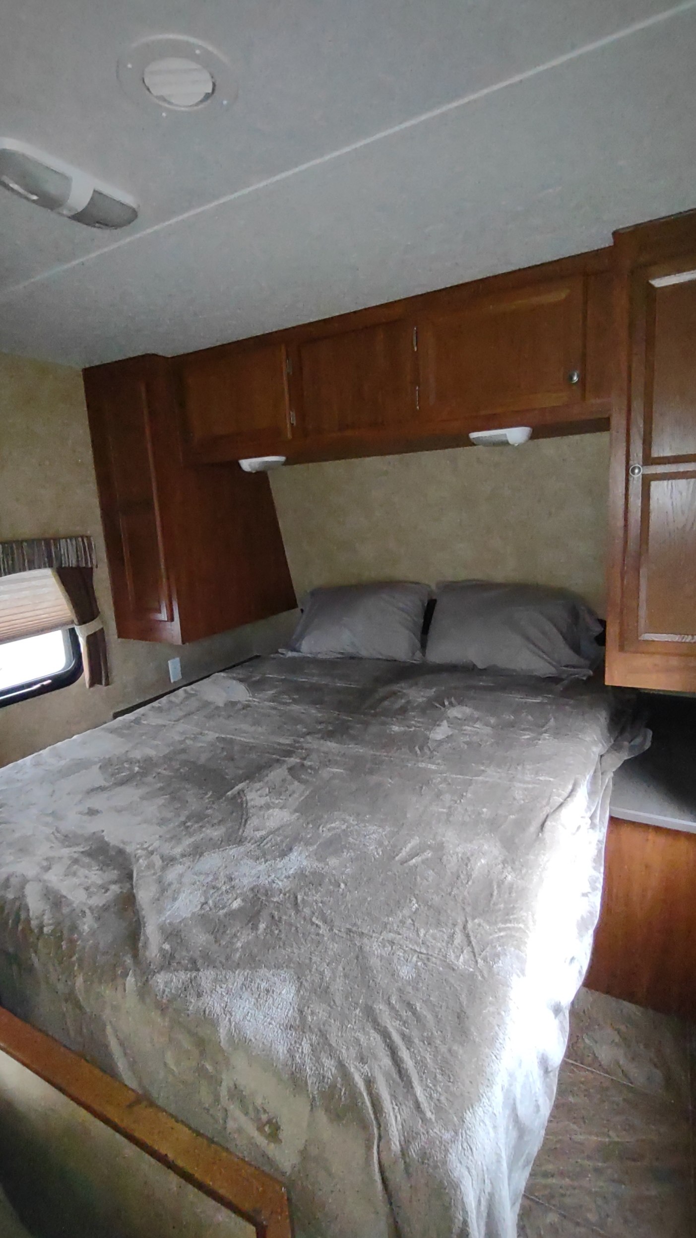 RV rental bedroom interior featuring a bed with grey linens, wood cabinets & a small window.. Jayco Jay Flight Swift 2012
