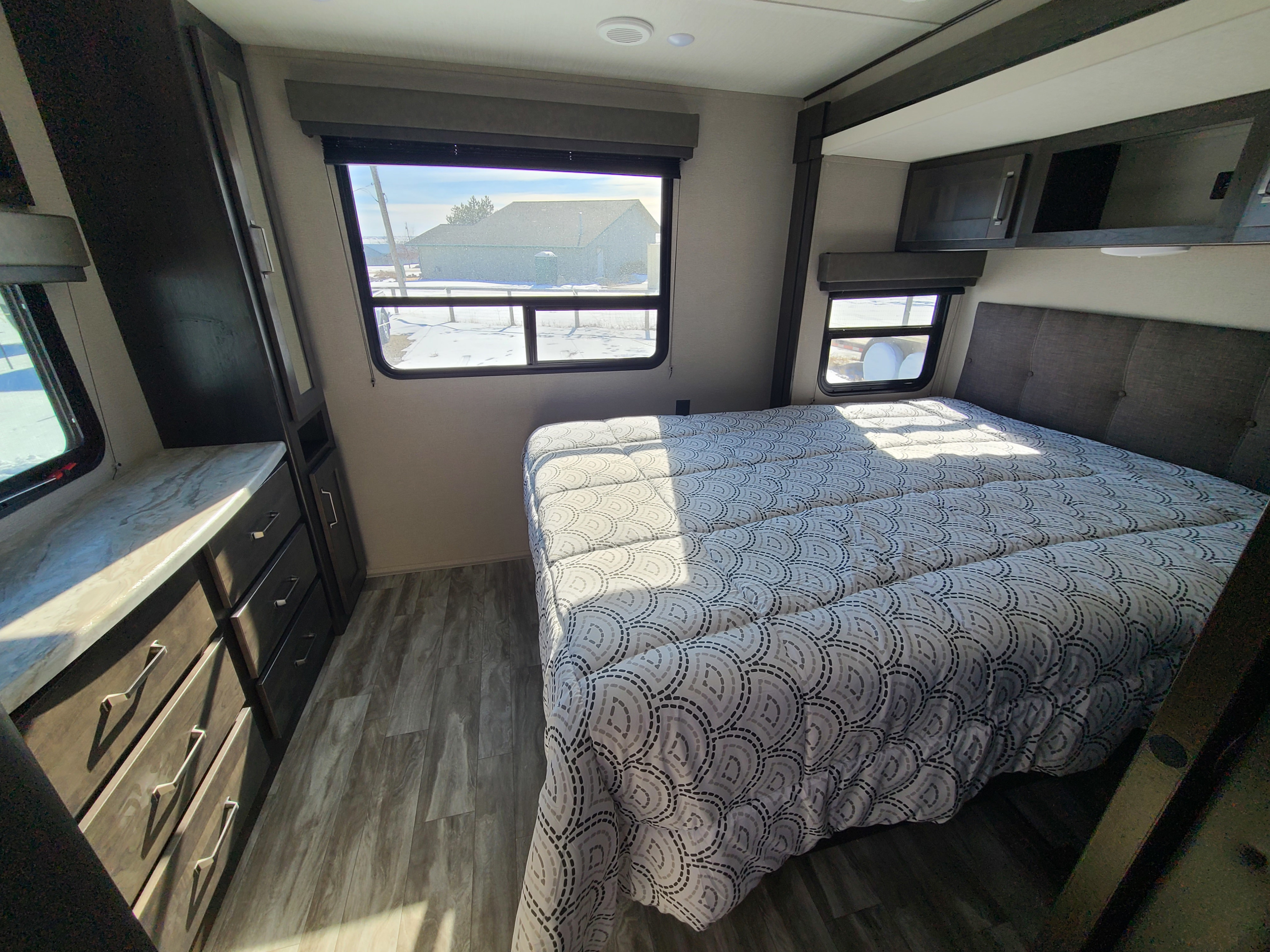 Explore this cozy RV rental bedroom featuring a comfy bed with modern patterned comforter, built-in storage, and bright windows.. Grand Design Transcend Xplor 2022