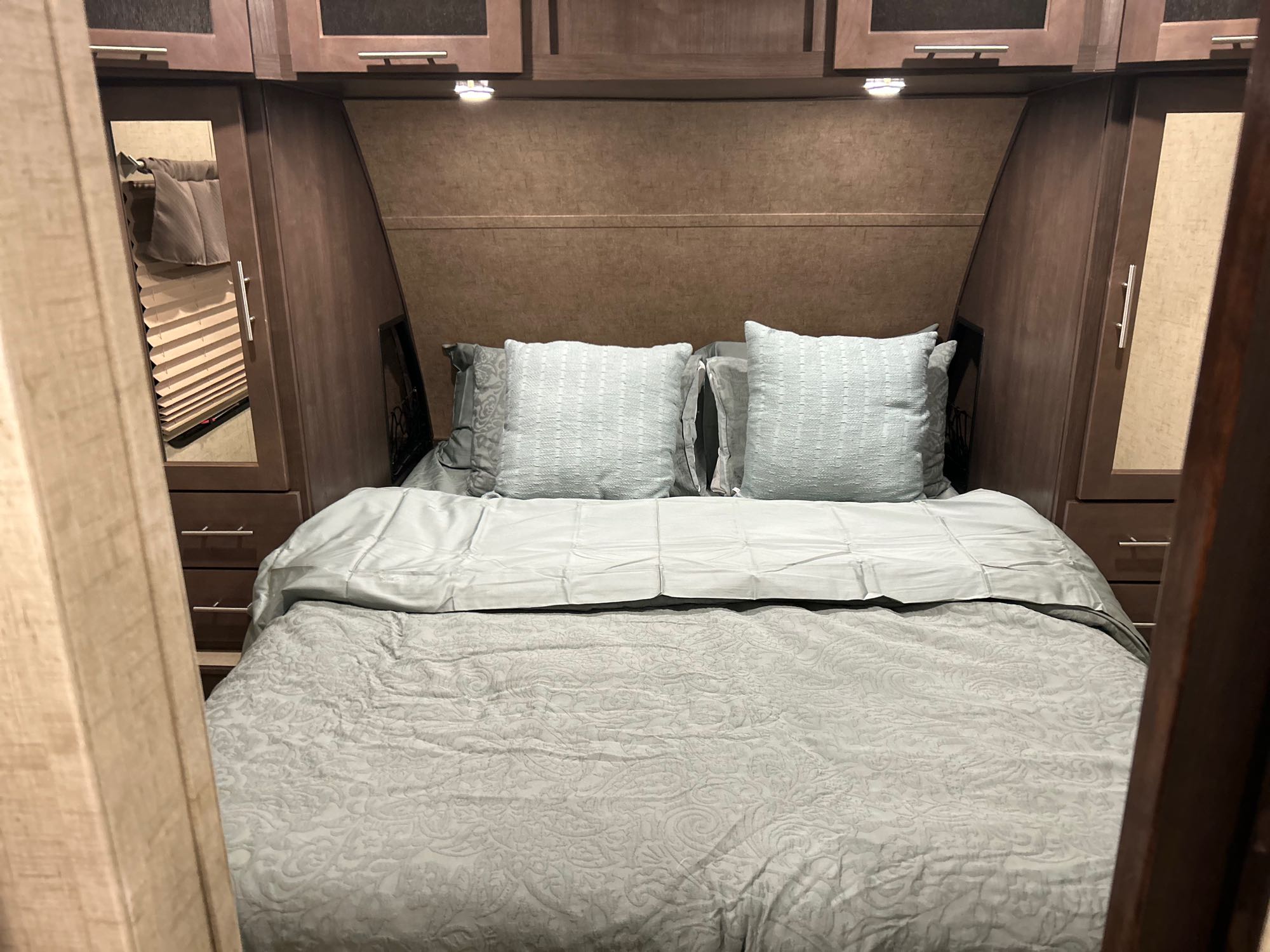 Cozy RV rental bedroom with a neatly made bed, overhead cabinets, and built-in side storage for a comfortable stay.. Forest River Surveyor 2016