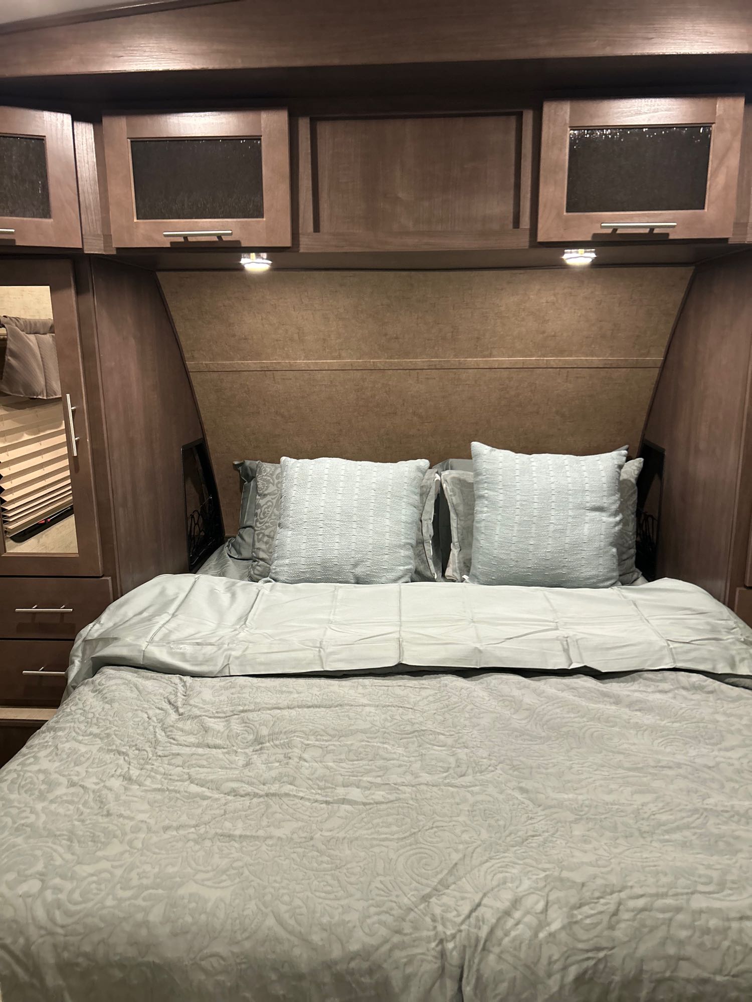 RV rental bedroom: Bed with light blue linens, overhead wood cabinets, and integrated side storage. Compact space.. Forest River Surveyor 2016