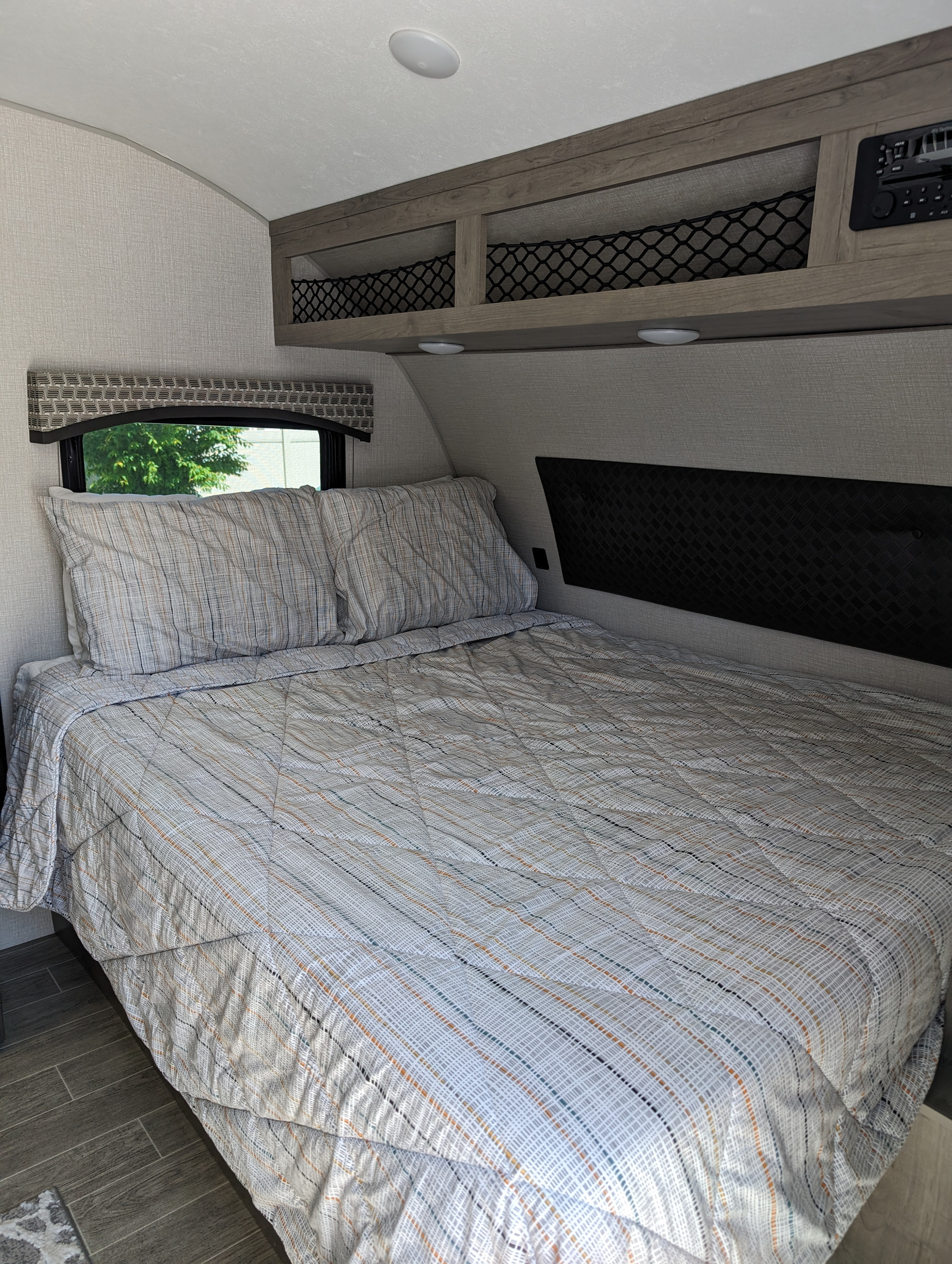 Inviting RV rental bedroom: bed with striped bedding, overhead storage with mesh, window, and wood-look floors.. Sonic Lite 2021