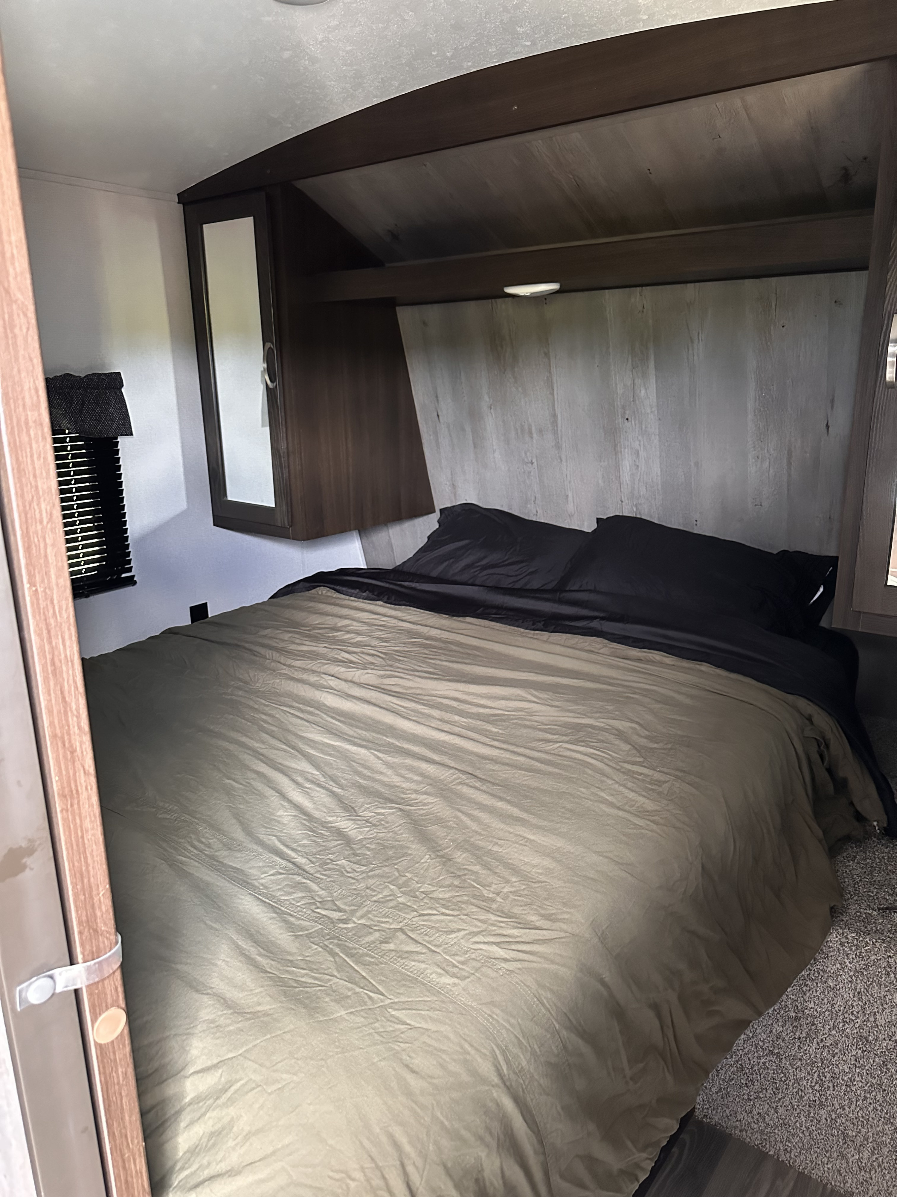 Cozy RV rental bedroom featuring an olive bed with black pillows, built-in storage, and a headboard. Ideal for travelers.. Keystone RV Springdale 2020