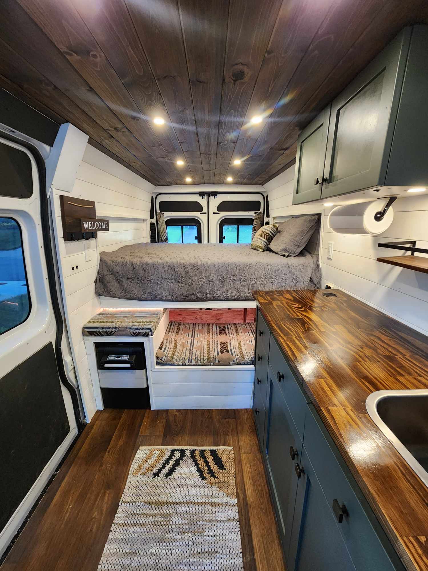 Detailed RV rental interior: raised bed, kitchen, wood ceiling, and white walls in a modern camper van conversion.. Dodge 1500 2014