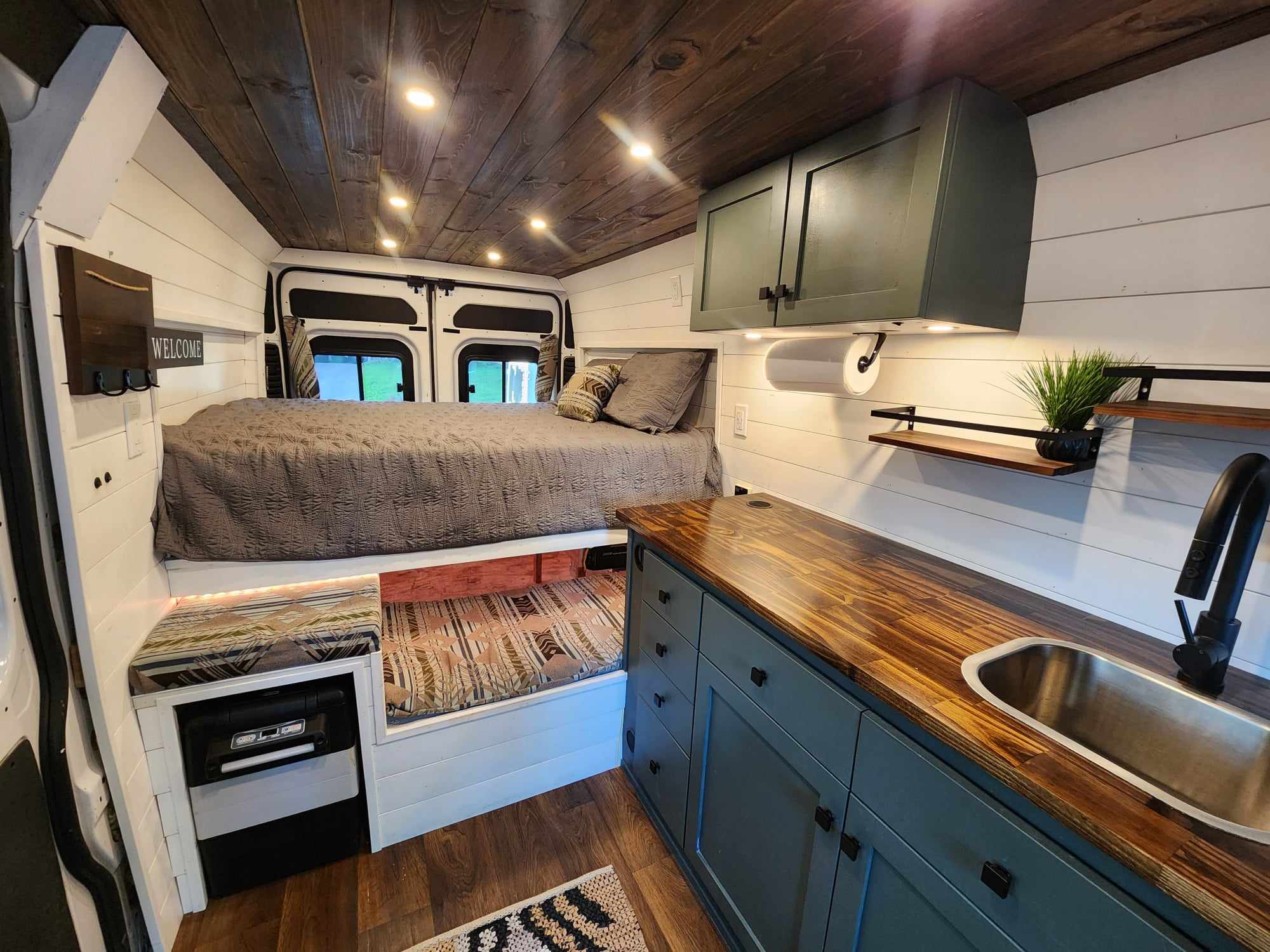 Inside a cozy RV rental: custom van conversion with raised bed, lower bunk/seating, kitchen w/sink, and stylish wood details.. Dodge 1500 2014