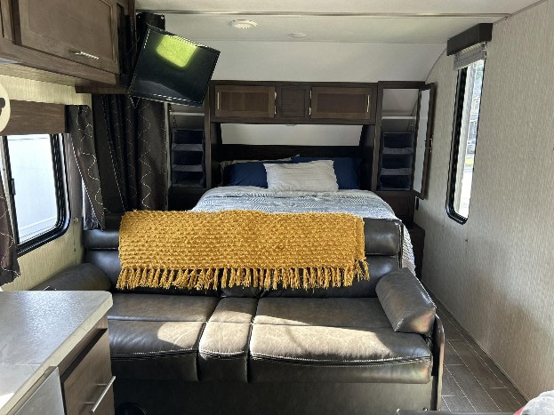RV rental interior: cozy bed, sofa with yellow blanket, & TV. Perfect travel trailer living space for your trip.. Forest River Cherokee Grey Wolf Special Edition 2020
