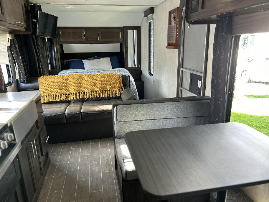Inside a modern RV rental: a bedroom with a yellow blanket, lounge area, dining booth, and compact kitchen.. Forest River Cherokee Grey Wolf Special Edition 2020