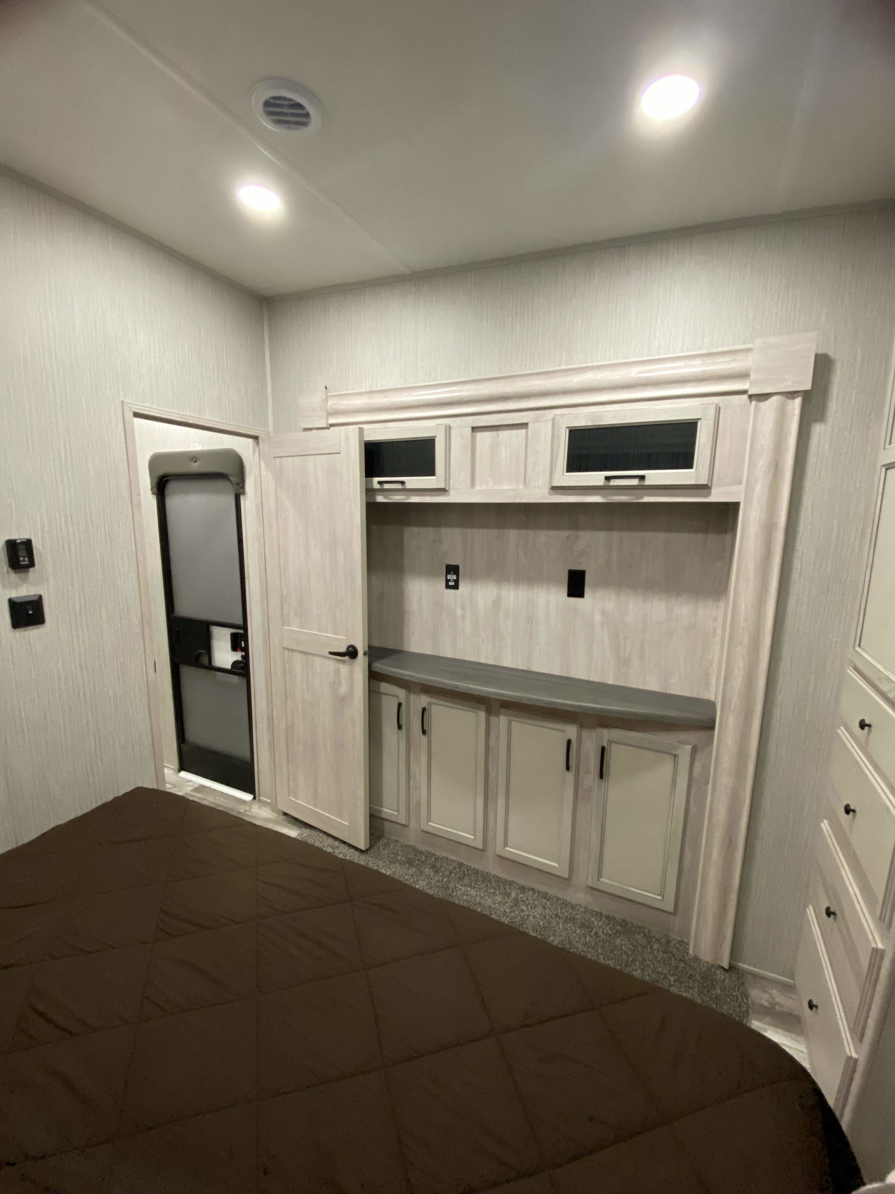 Comfortable RV rental bedroom with brown bed, built-in light wood storage, door, and controls. A compact, inviting space.. Forest River Other 2022