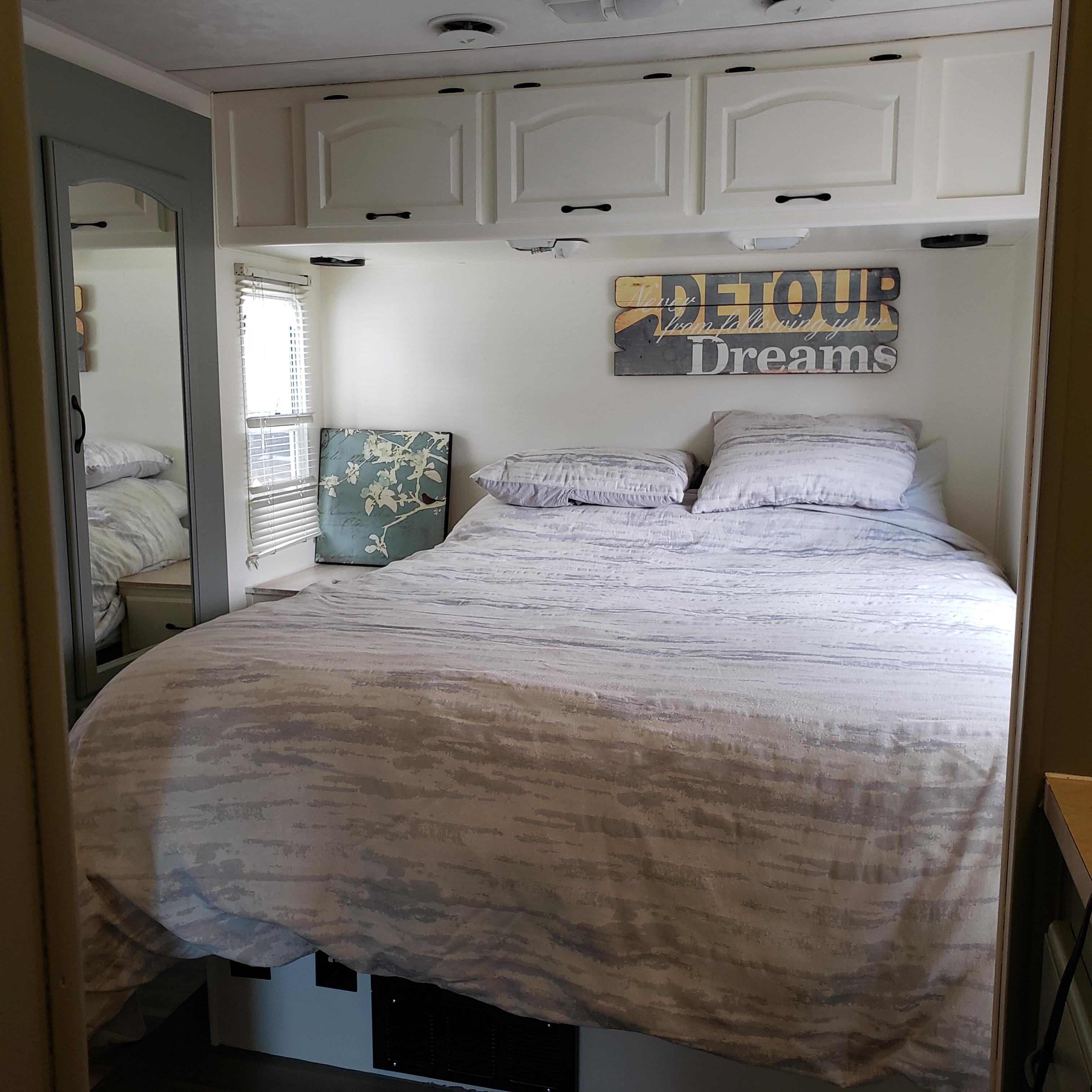 Cozy RV rental bedroom featuring patterned bedding, overhead cabinets, a side mirror, and a window with blinds for travel comfort.. Damon Corporation Daybreak 2002