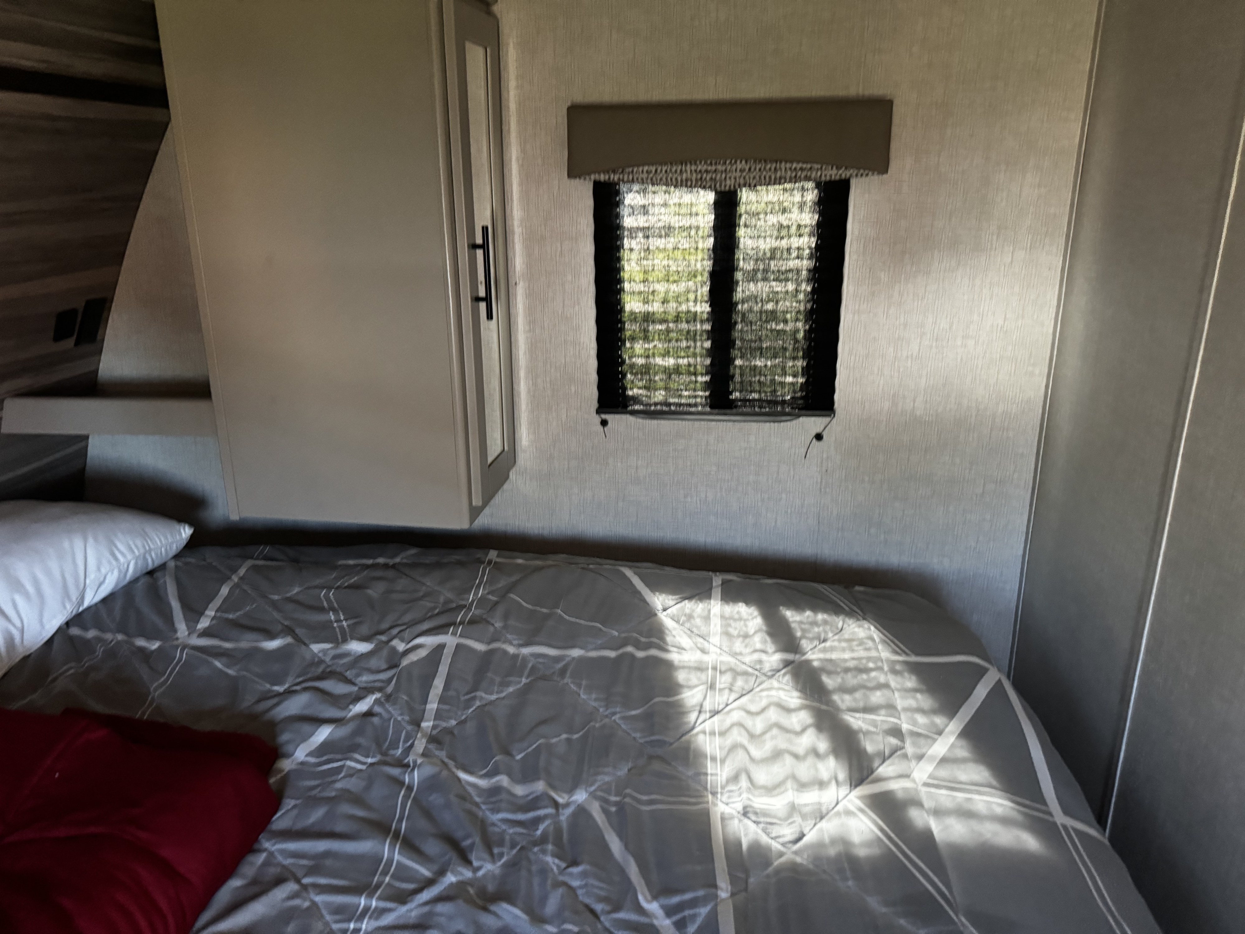 Cozy RV rental bedroom with a grey patterned bed, a small window with blinds, and a light-colored storage cabinet.. Crossroads RV Cruiser Aire 2021