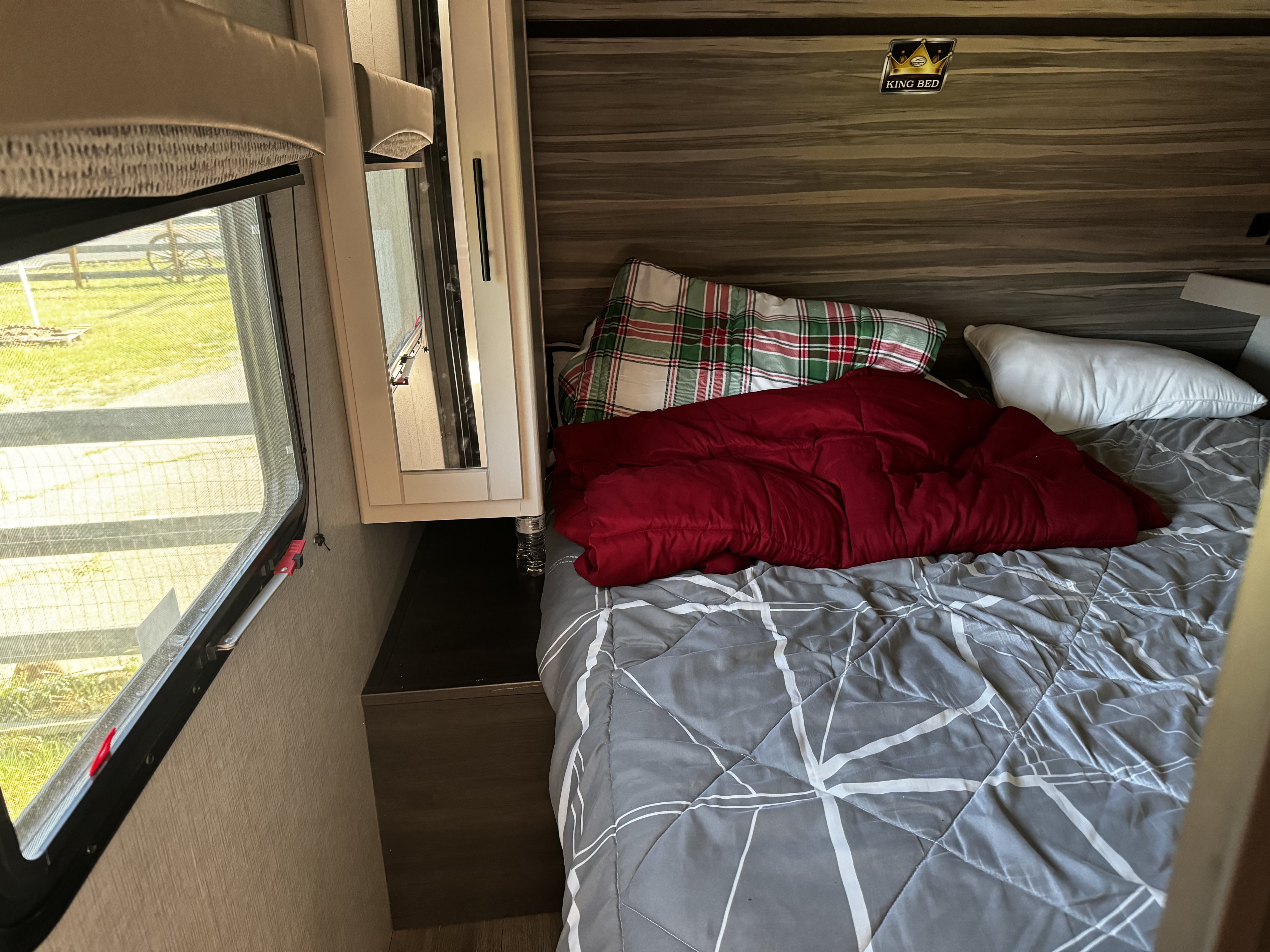 Cozy RV rental bedroom featuring a King bed with plaid and red bedding, window view, and mirrored cabinet.. Crossroads RV Cruiser Aire 2021