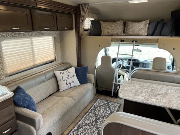 Cozy RV rental interior features a comfy living area with sofa, overhead bunk with ladder, and dinette.. Thor Freedom Elite 2017