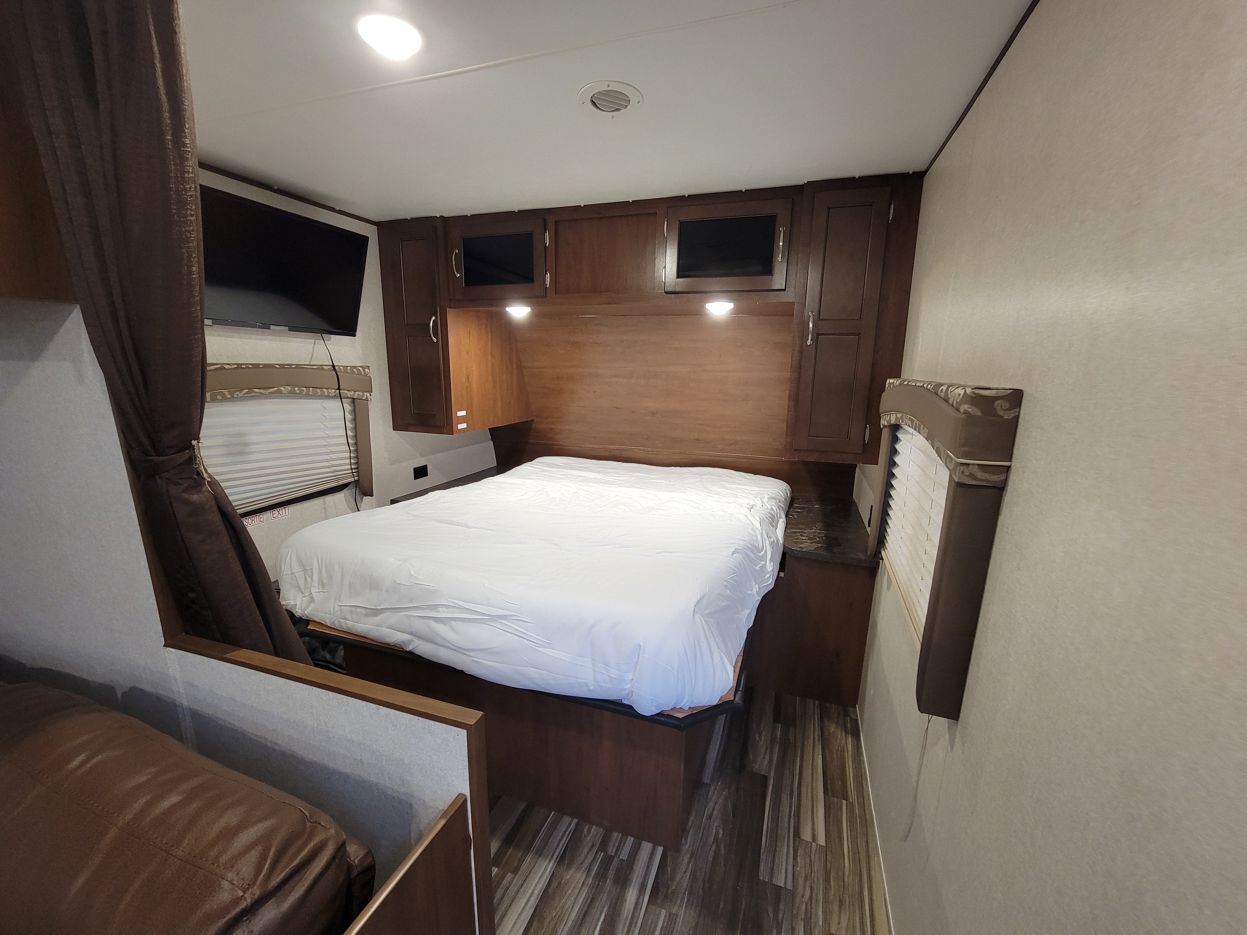 RV rental bedroom interior featuring a queen bed, mounted TV, and ample wood cabinets for storage.. jayco Jayflight 2017