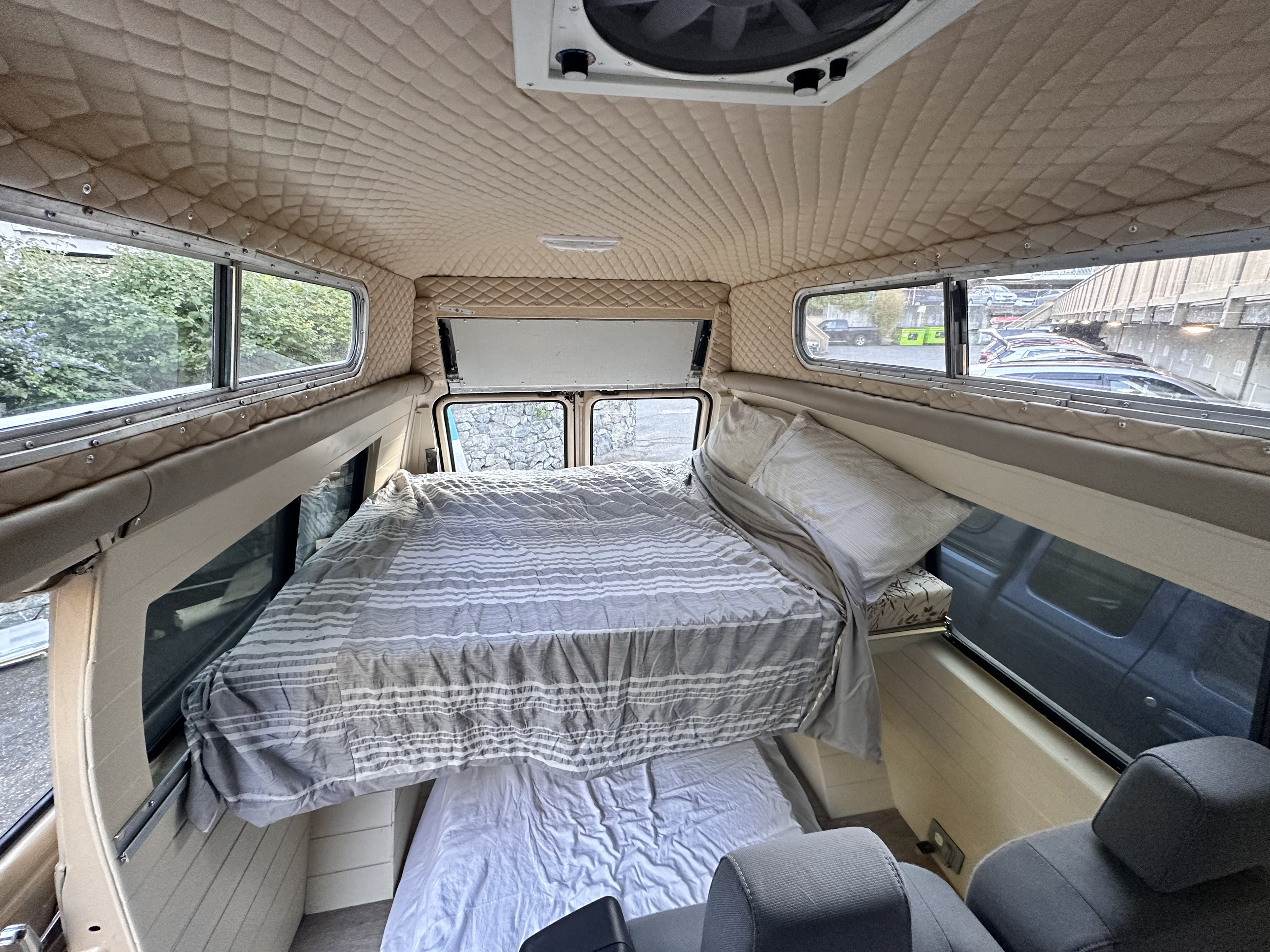 Cozy RV rental interior, showcasing a sleeping area with a raised bed, lower mattress, and quilted ceiling for comfort.. Chevrolet G10 High Top Van 1984