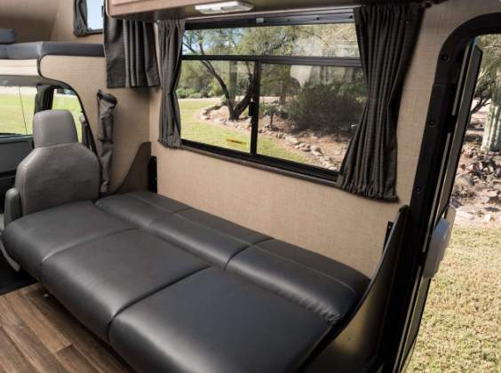 RV rental interior: convertible sofa bed, window with curtains, and overhead bunk. Ideal for travel comfort.. Thor Majestic 2019