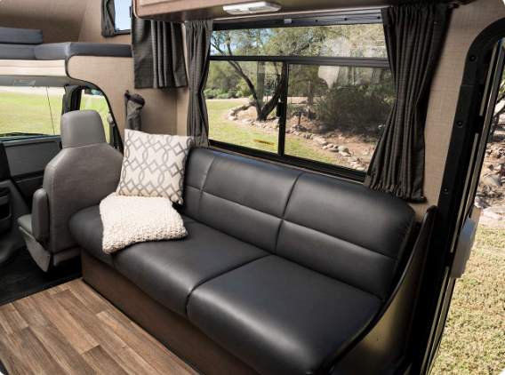 Enjoy your RV rental! Cozy living space with a black sofa, decorative pillows, wood-look floor, and scenic window.. Thor Majestic 2019