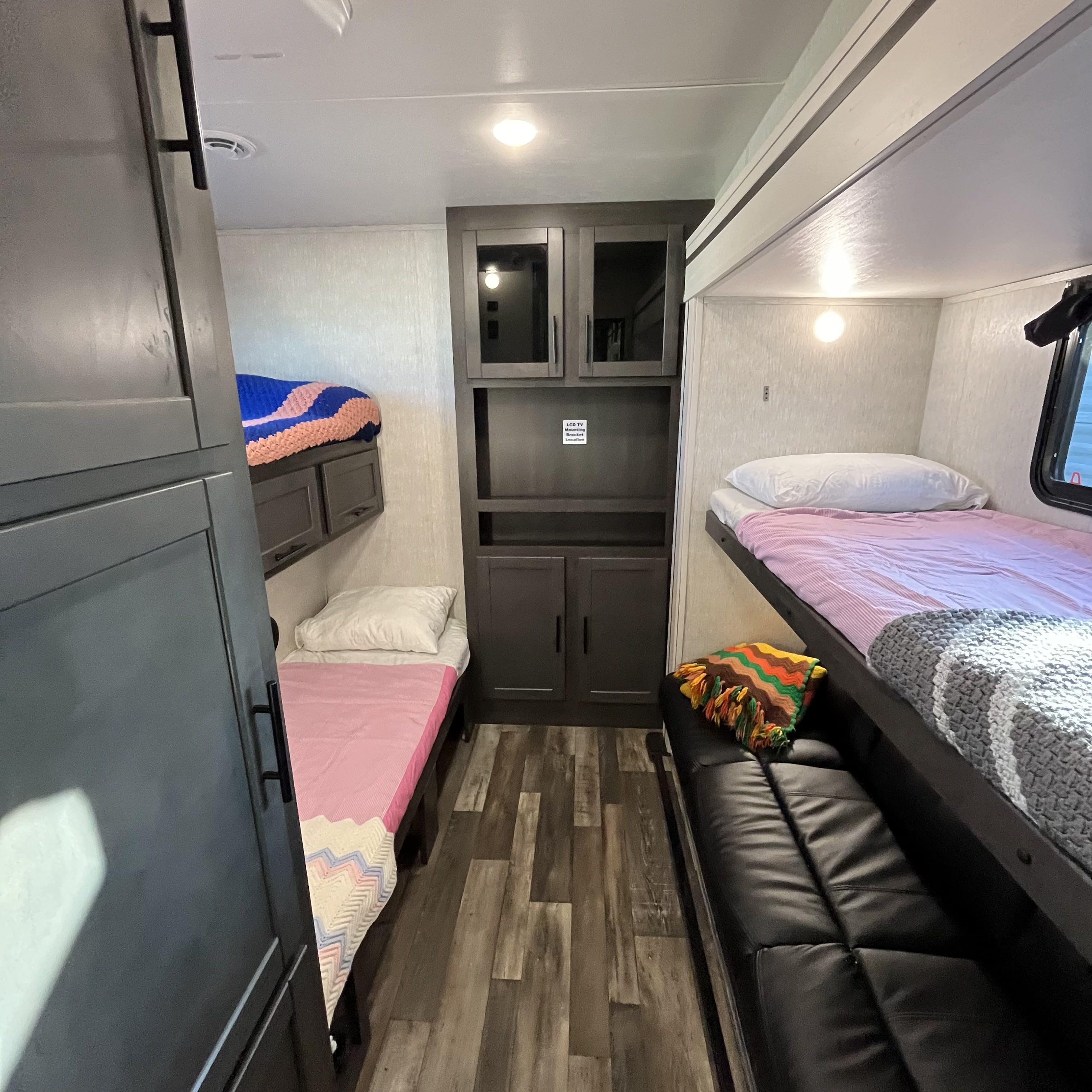 Cozy RV rental bunk room features multiple beds, central storage cabinets, and a compact lounge area for family comfort.. Crossroads Cruiser 2022