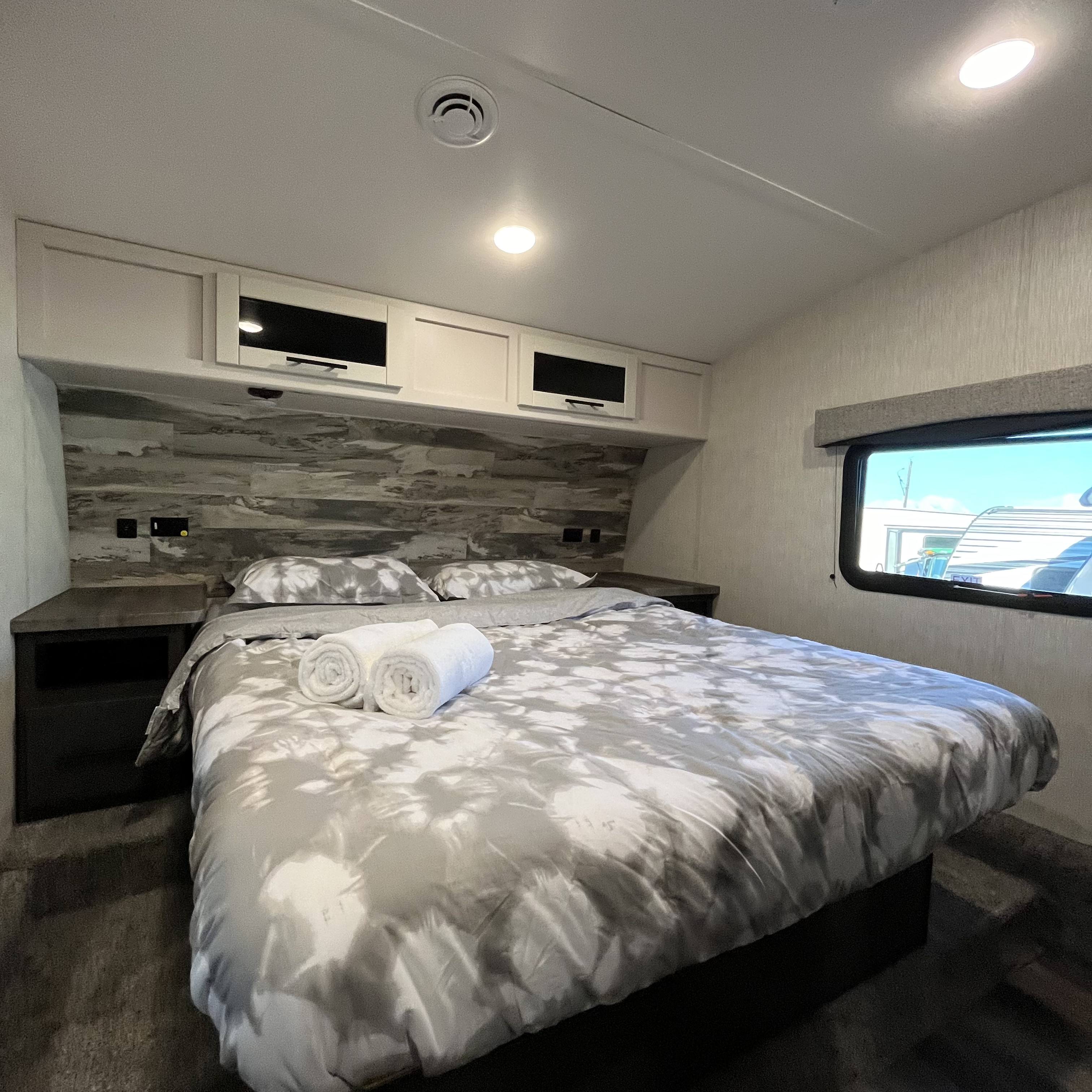 Inside an RV rental: a spacious bedroom featuring a comfortable bed with patterned linens, overhead cabinets, and a window view.. Crossroads Cruiser 2022