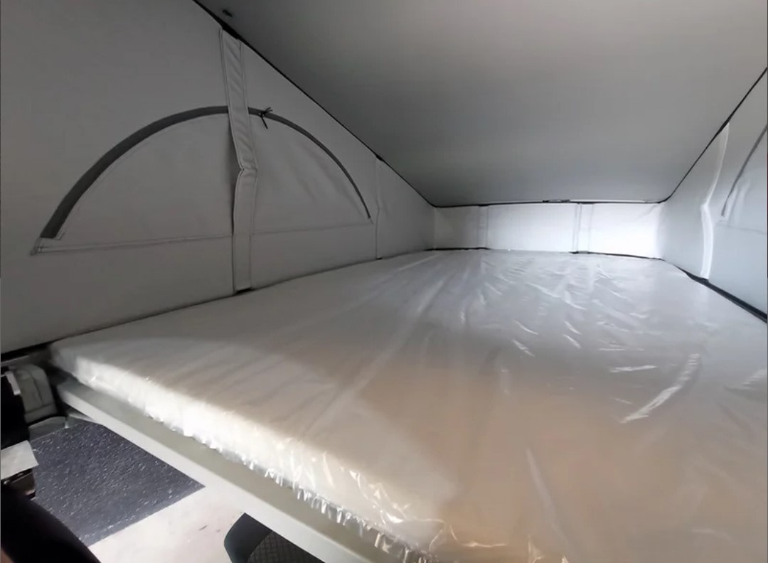 Inside an RV rental: a bright pop-top sleeping area with a new, plastic-wrapped mattress, ready for rest.. Volkswagen California Beach Camper 2.0 TDI 2023