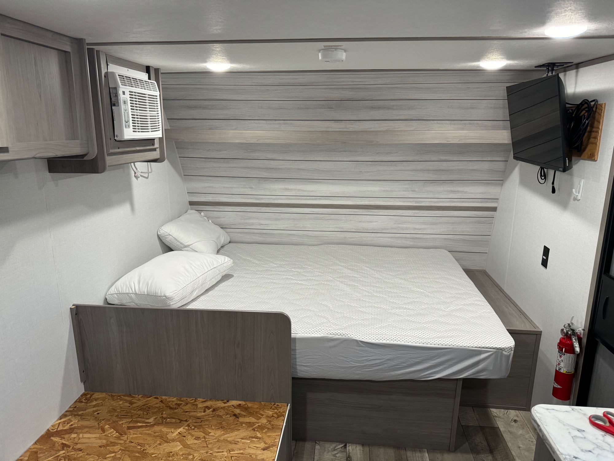 Cozy RV rental bedroom showing a bed, wall-mounted AC, TV, and safety equipment like a fire extinguisher.. Coleman 17B 2024