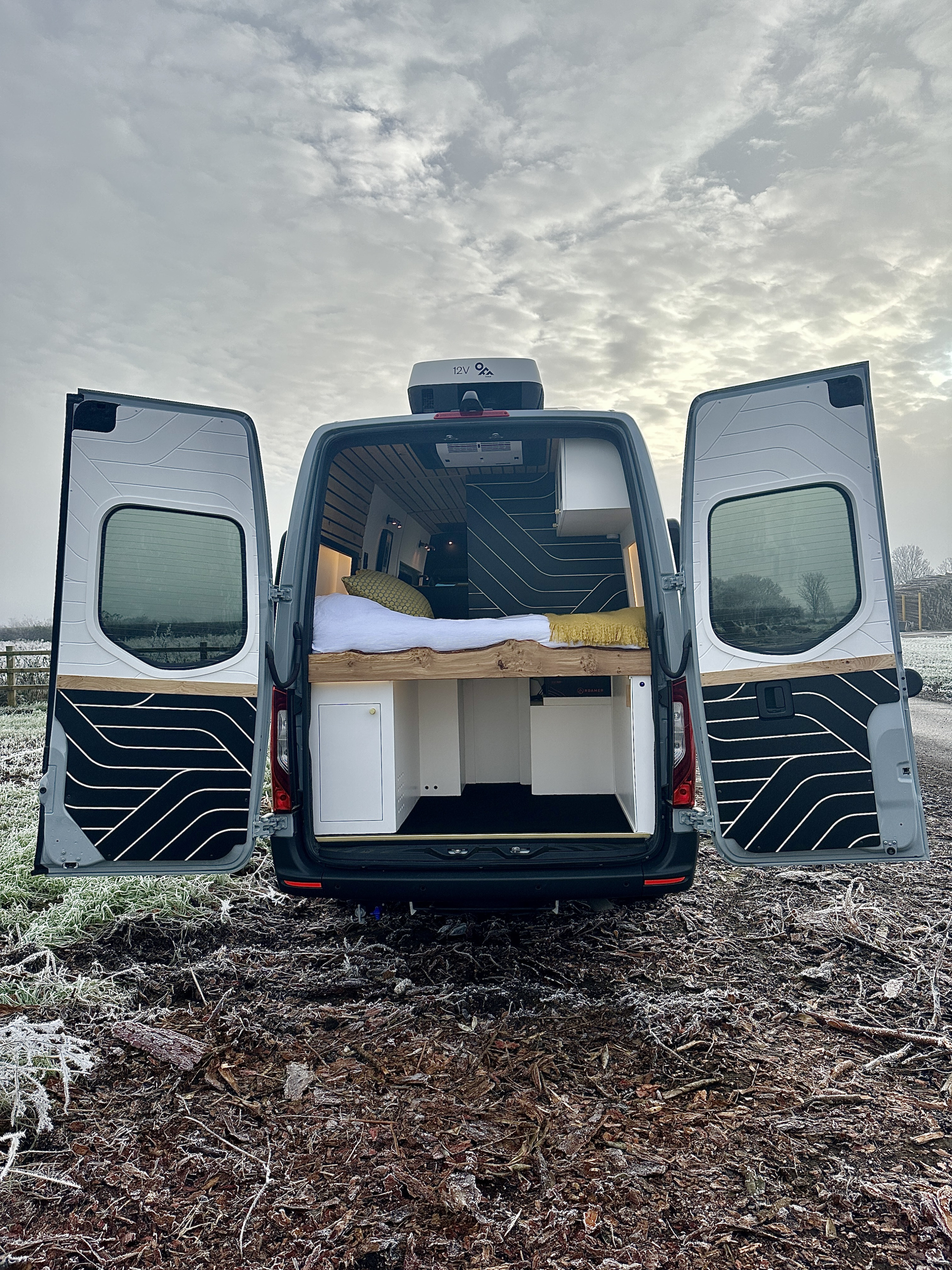 Inside a grey custom campervan. Open rear doors reveal a cozy bed & storage, ideal for an rv rental adventure.. Mercedes Benz Sprinter 2023