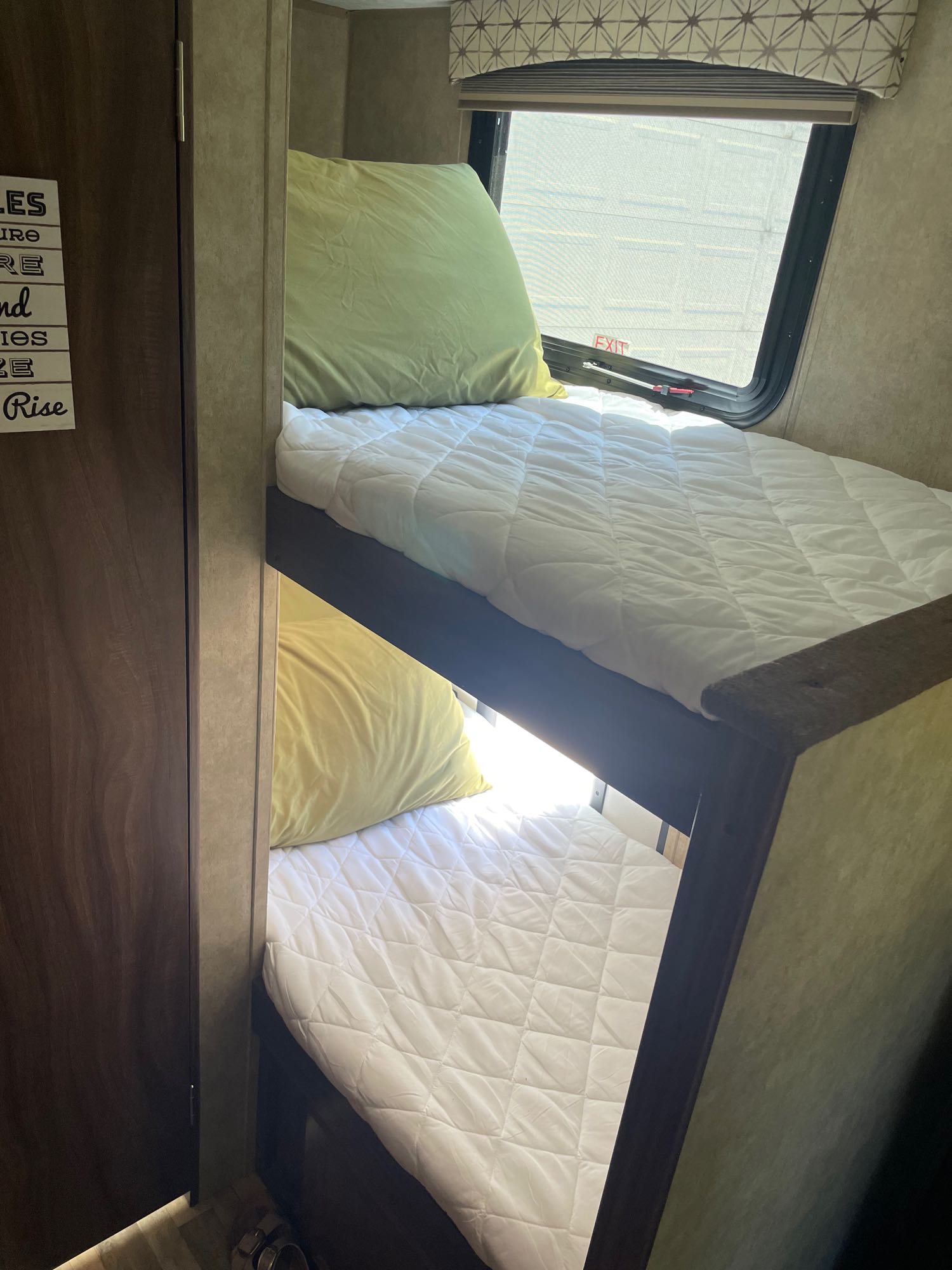 Inside an RV rental, two bunk beds with white quilted bedding and light pillows. An exit window is visible above the top bunk.. Forest River Viking 2018