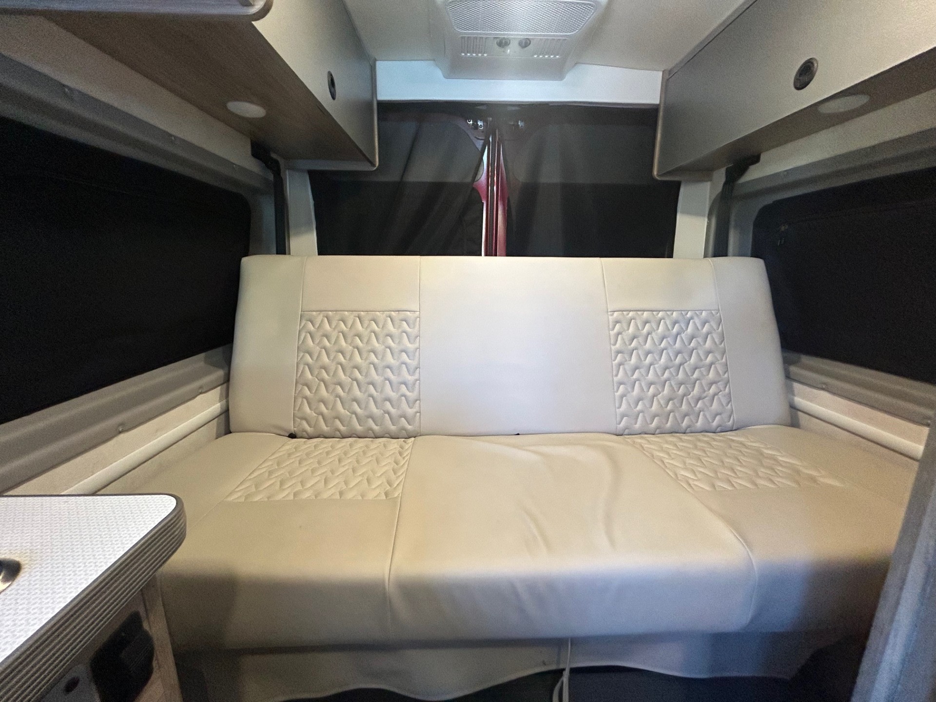 RV rental interior: Comfortable light-colored bench seat converts to a bed, with overhead storage and dark window coverings for privacy.. Winnebago Solis 2022