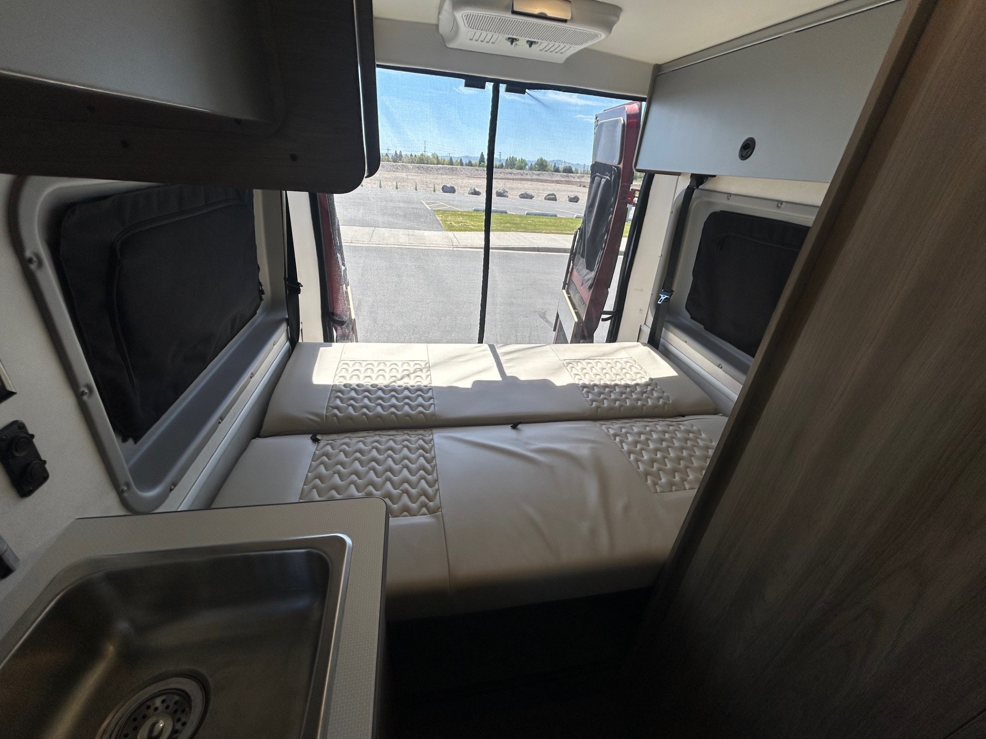 Spacious RV rental interior with a comfortable bed, compact sink, and rear doors open to the scenic view.. Winnebago Solis 2022
