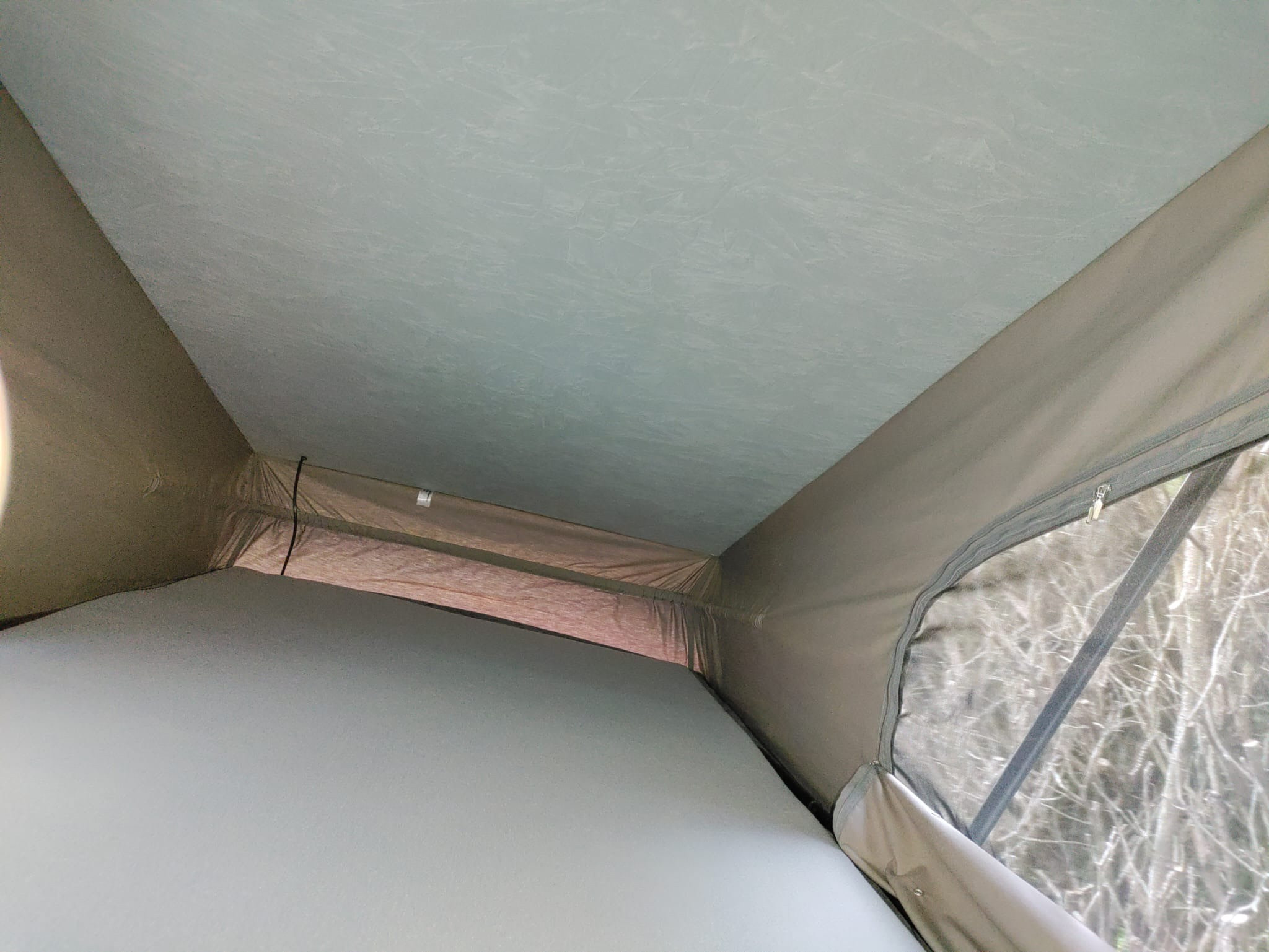 Interior of an RV rental pop-top camper, showing the sleeping area and a zipped window revealing bare trees outside.. Volkswagen Style California 2014