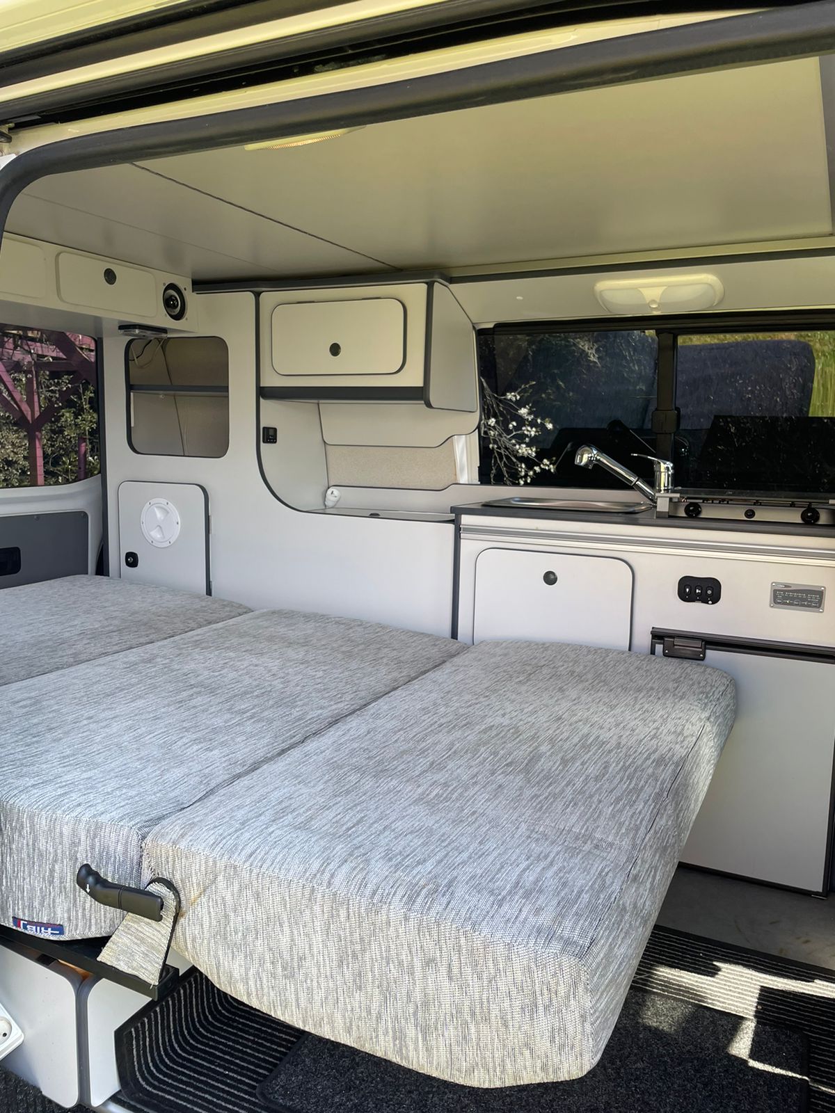Interior of compact RV rental: features light grey bed, built-in kitchenette with sink and stove, plus storage units.. Volkswagen Style California 2014
