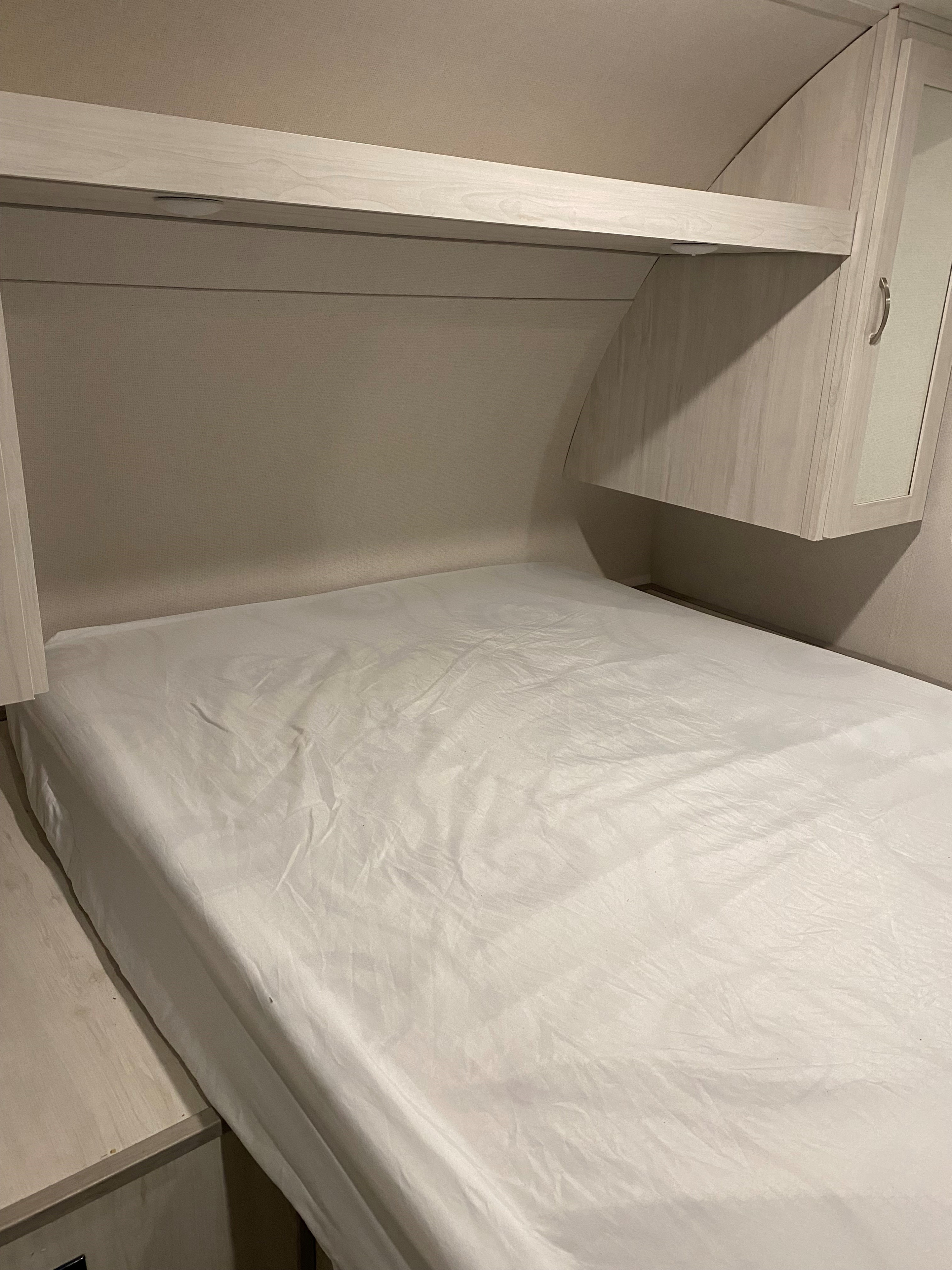 RV rental bedroom interior with light wood overhead storage, a small reading light, and a fresh white bed.. Forest River Tracer LE 2022