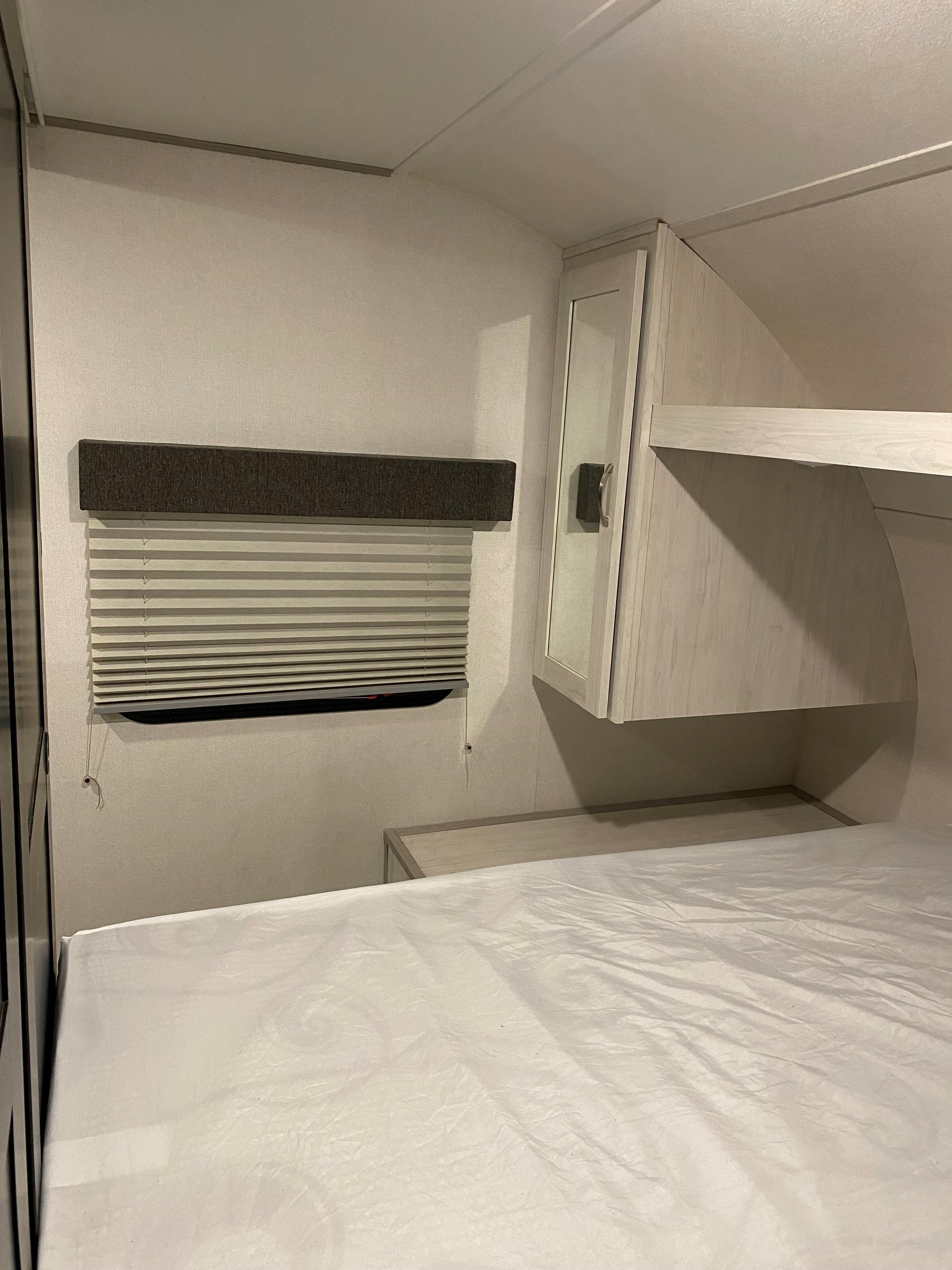 Cozy RV rental bedroom featuring a clean bed, window blinds, and built-in light wood cabinets with a mirrored door.. Forest River Tracer LE 2022