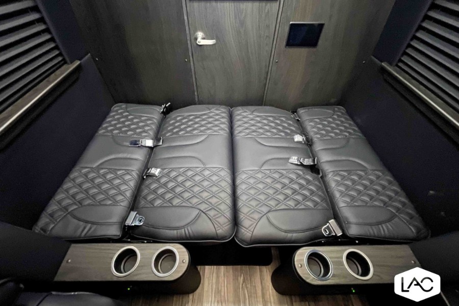 Luxury RV rental interior: plush, diamond-quilted seats laid flat as a bed, with cup holders and a sleek wooden door.. Midwest Automotive Designs Luxe Cruiser 2024