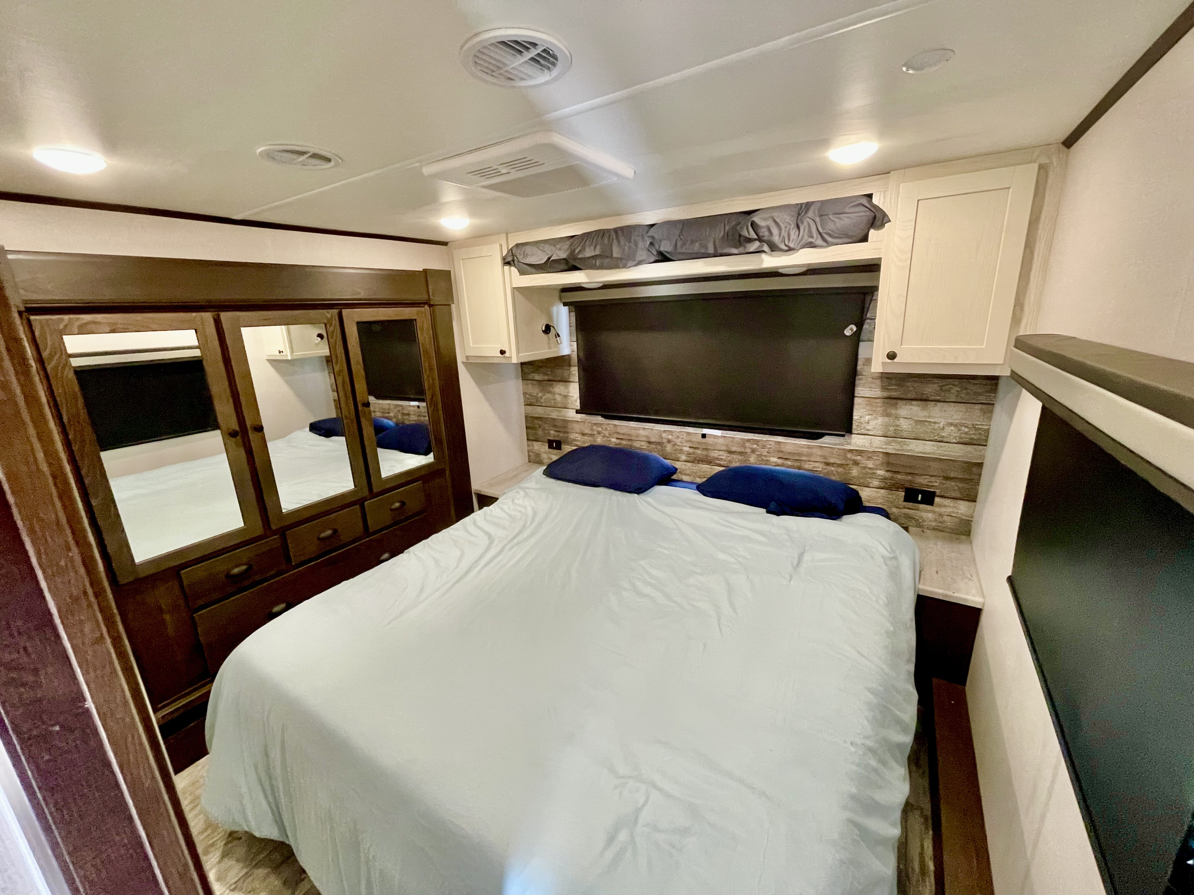 Cozy RV rental bedroom featuring a comfortable bed, mirrored wardrobe, overhead cabinets, and a wall-mounted TV.. Forest River XLR Nitro Toy Hauler 2022