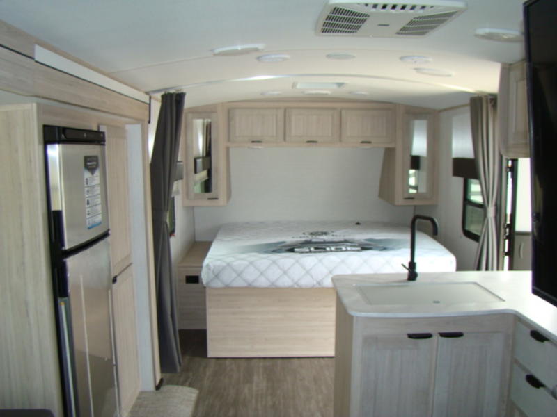 Modern RV rental interior featuring a comfortable bed, compact kitchen with sink, and refrigerator.. Cruiser RV Shadow Cruiser 2023