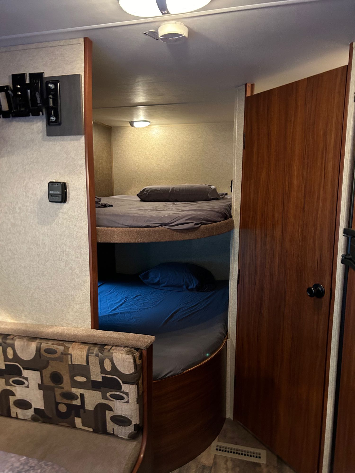 RV rental interior with cozy bunk beds (gray & blue bedding), a patterned dining bench, TV mount, and thermostat.. Heartland RVs Trail Runner 2014