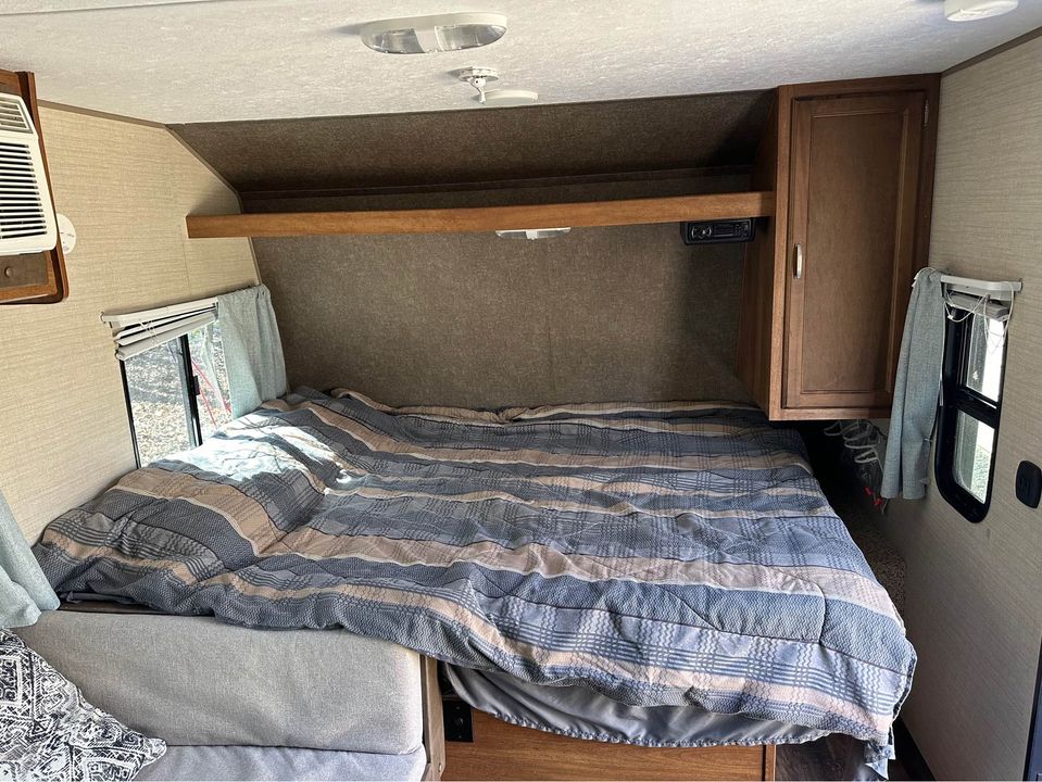 Spacious RV rental bedroom featuring a large bed with striped comforter, windows, AC, and storage. Ideal for travel comfort.. Keystone RV Summerland Mini 2017