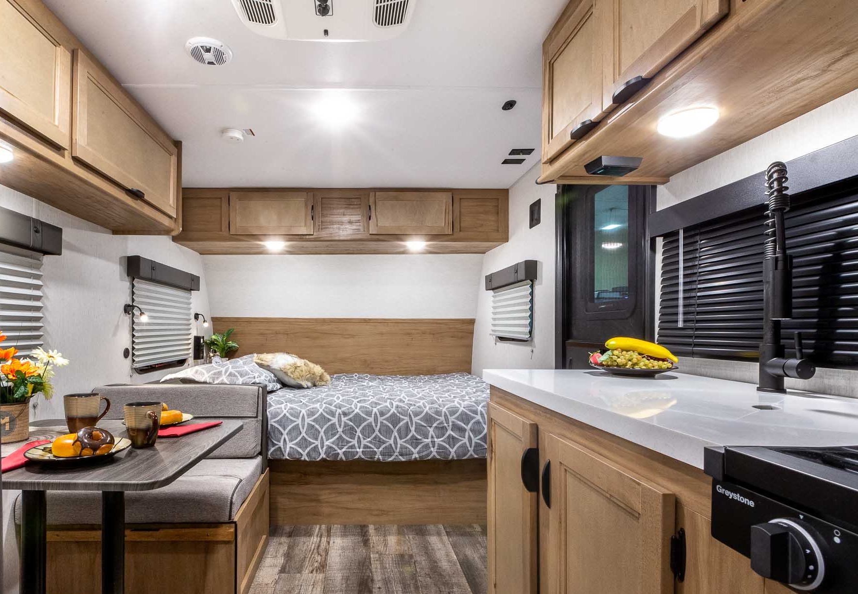 Cozy RV rental interior featuring a bed, dining booth, and kitchen area with light wood finishes. Ideal for compact travel adventures.. Forest River Cherokee Wolf Pup 2024