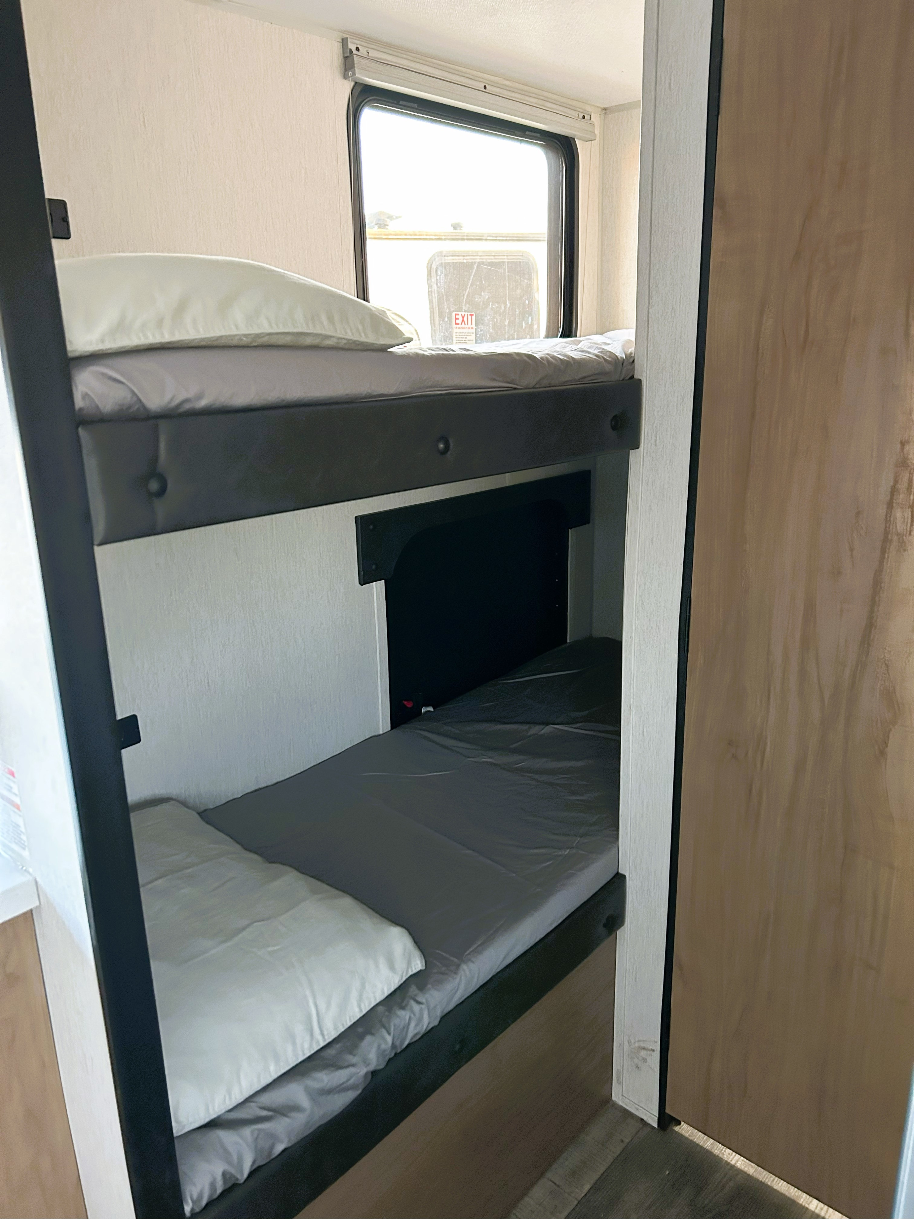 An RV rental features two practical bunk beds with light gray bedding, visible beside a window, offering compact sleeping quarters for travel.. Forest River Cherokee Wolf Pup 2023