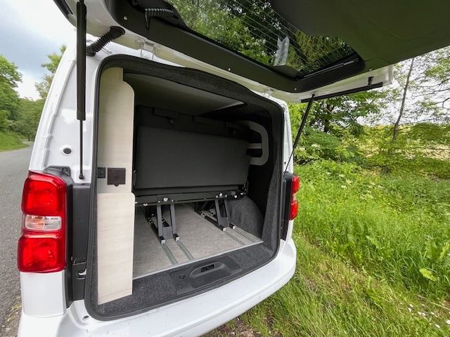 RV rental campervan with open tailgate revealing a compact, modular interior: a foldable bed/bench & side panel with outlets.. peugeot MyKitVan 2024